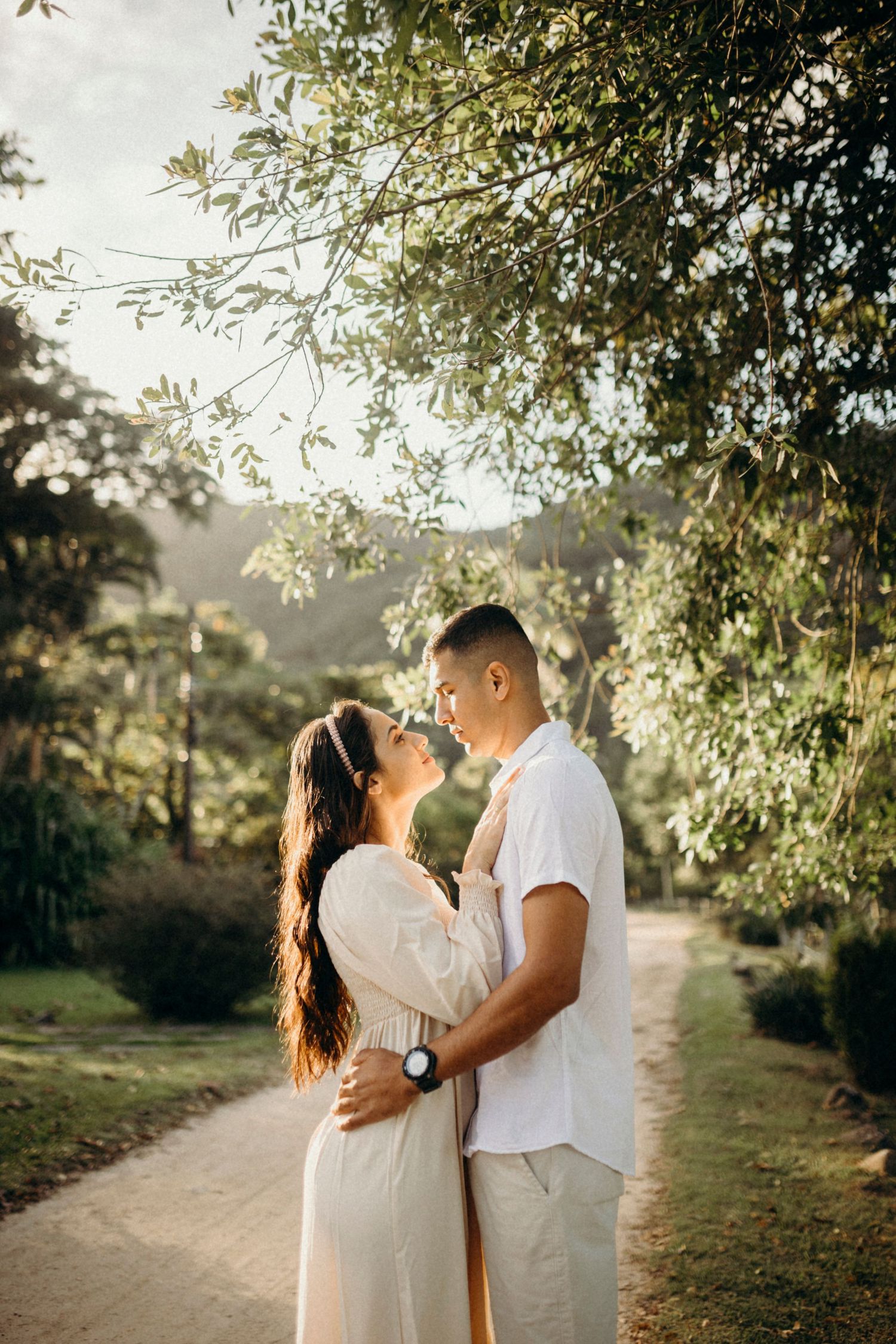 Couple in white attire embracing on a sunlit nature path.