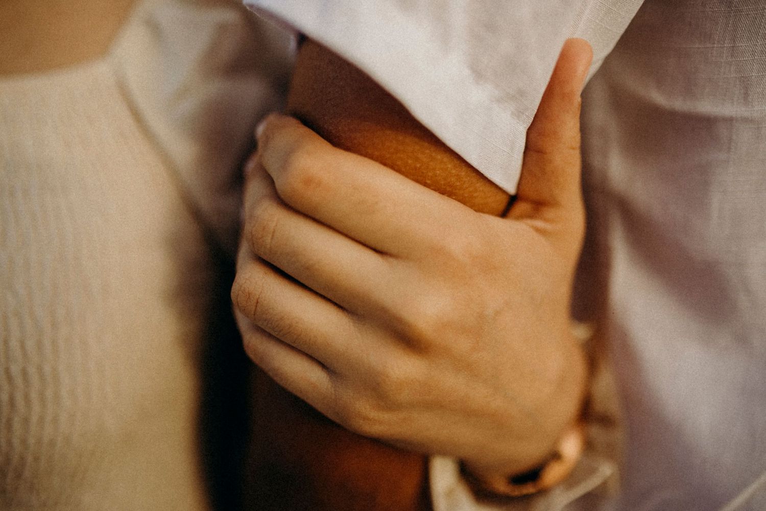 Close-up of hands tenderly embracing in white clothing.
