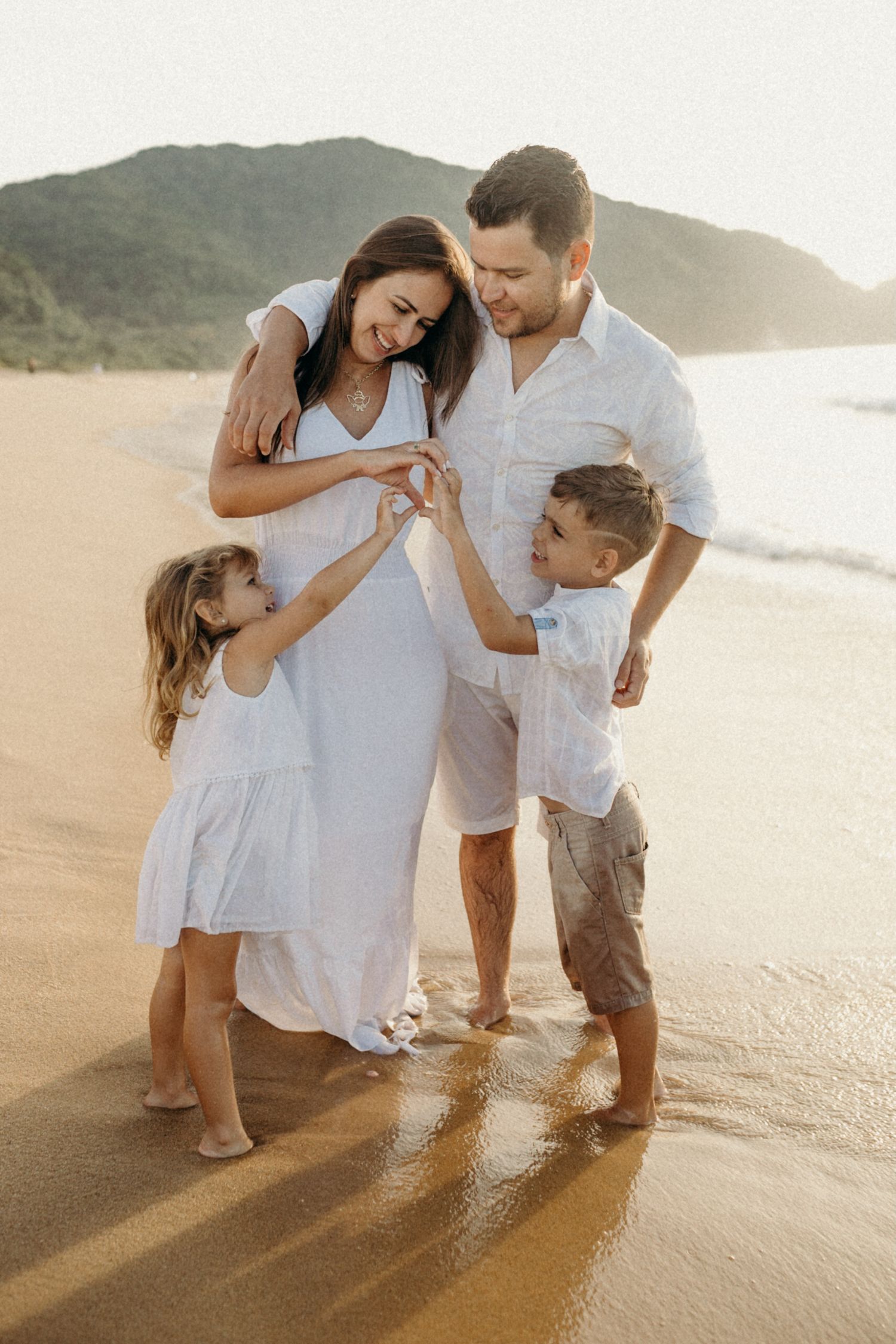 Family shares intimate moments while playing on a sandy beach at golden hour.