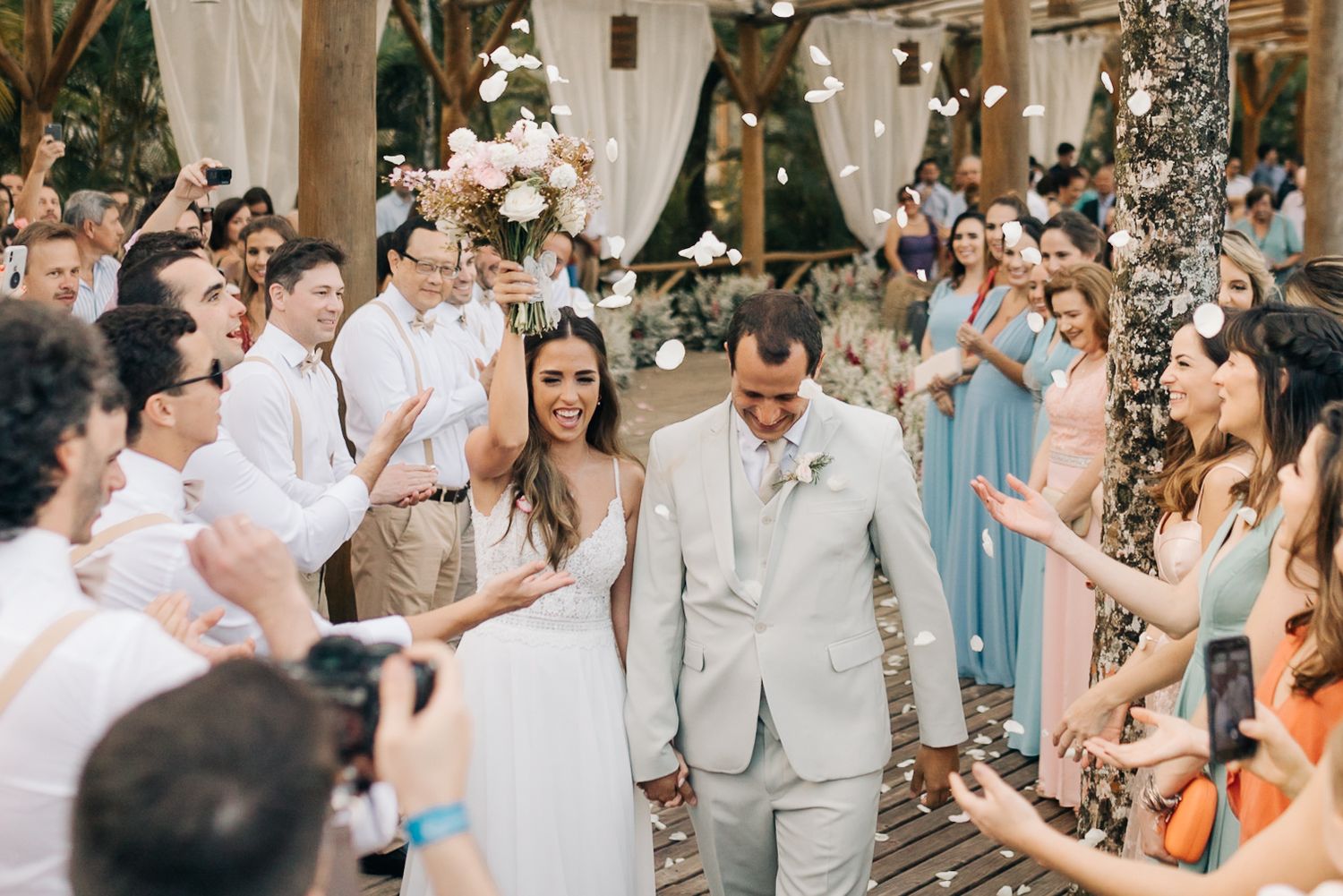 Wedding ceremony crowd celebrates under wooden beamed structure with natural lighting.