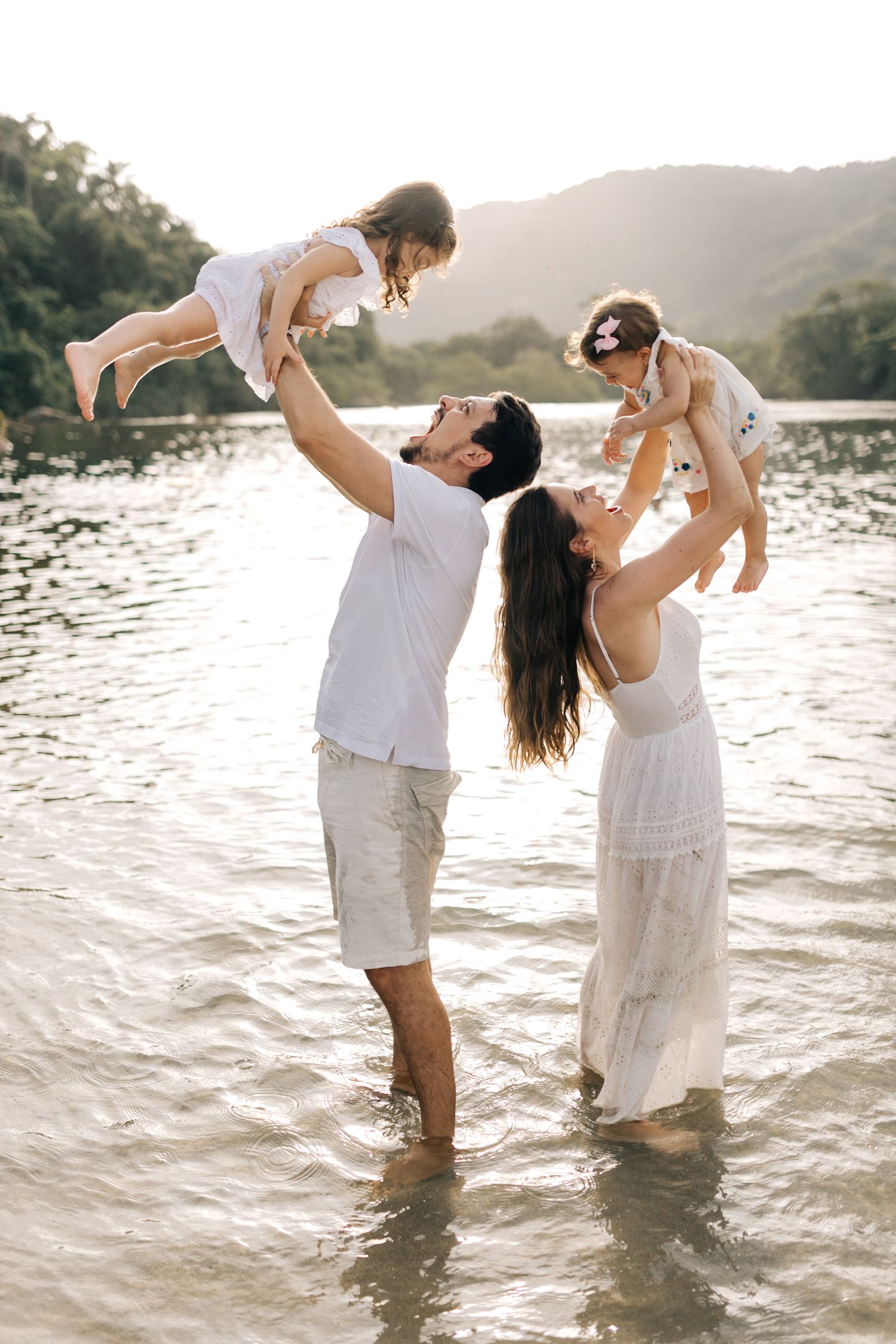 Happy family playing and lifting in ocean waves during golden hour photography session.
