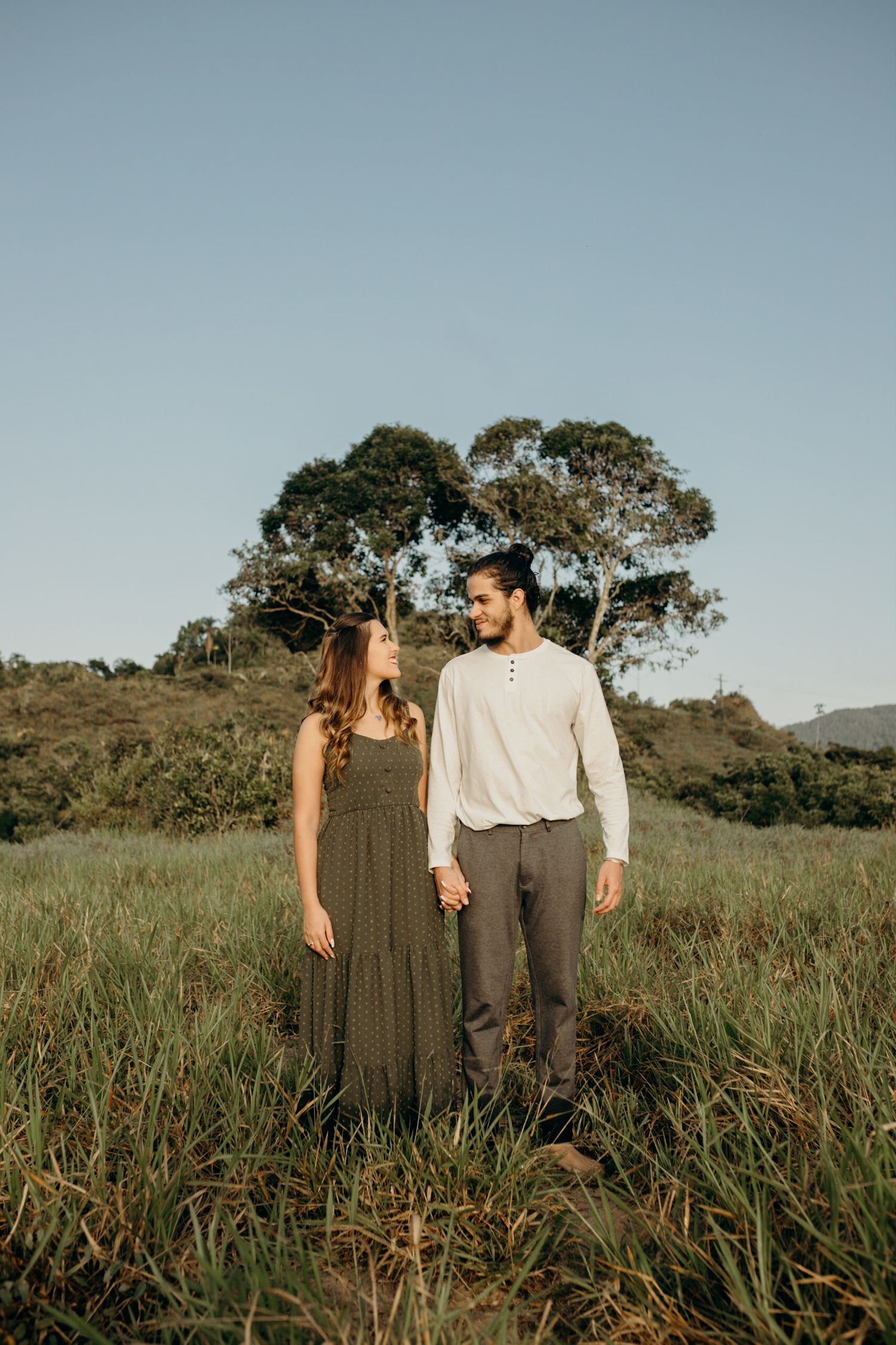 Couple walking together through tall grass in a natural outdoor setting at sunset.