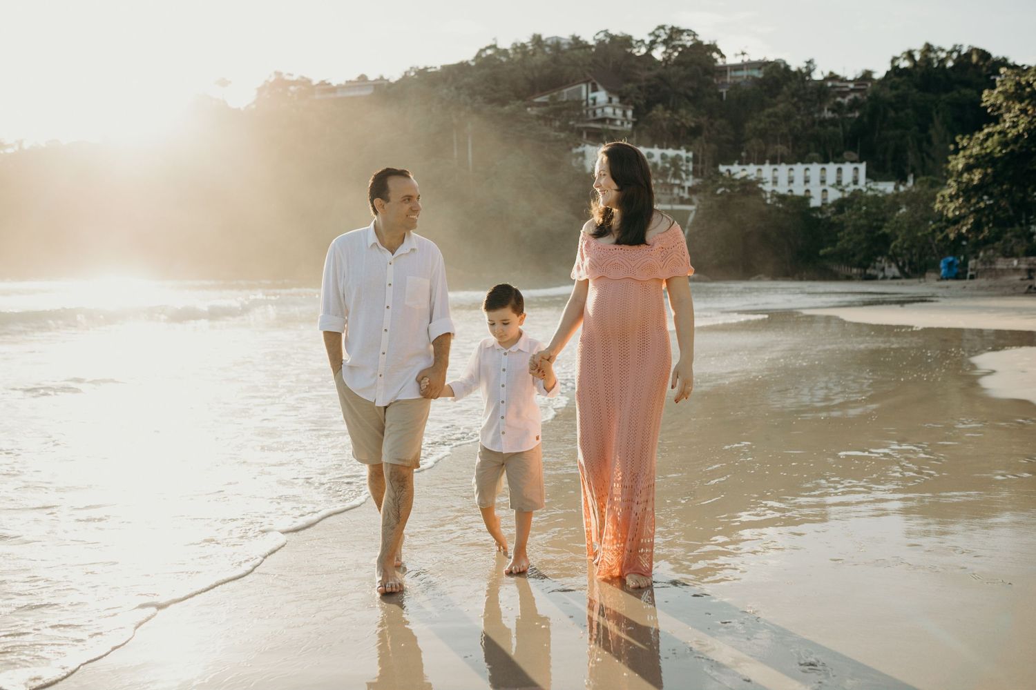 A family of three takes a sunset stroll along the shoreline of a scenic beach.