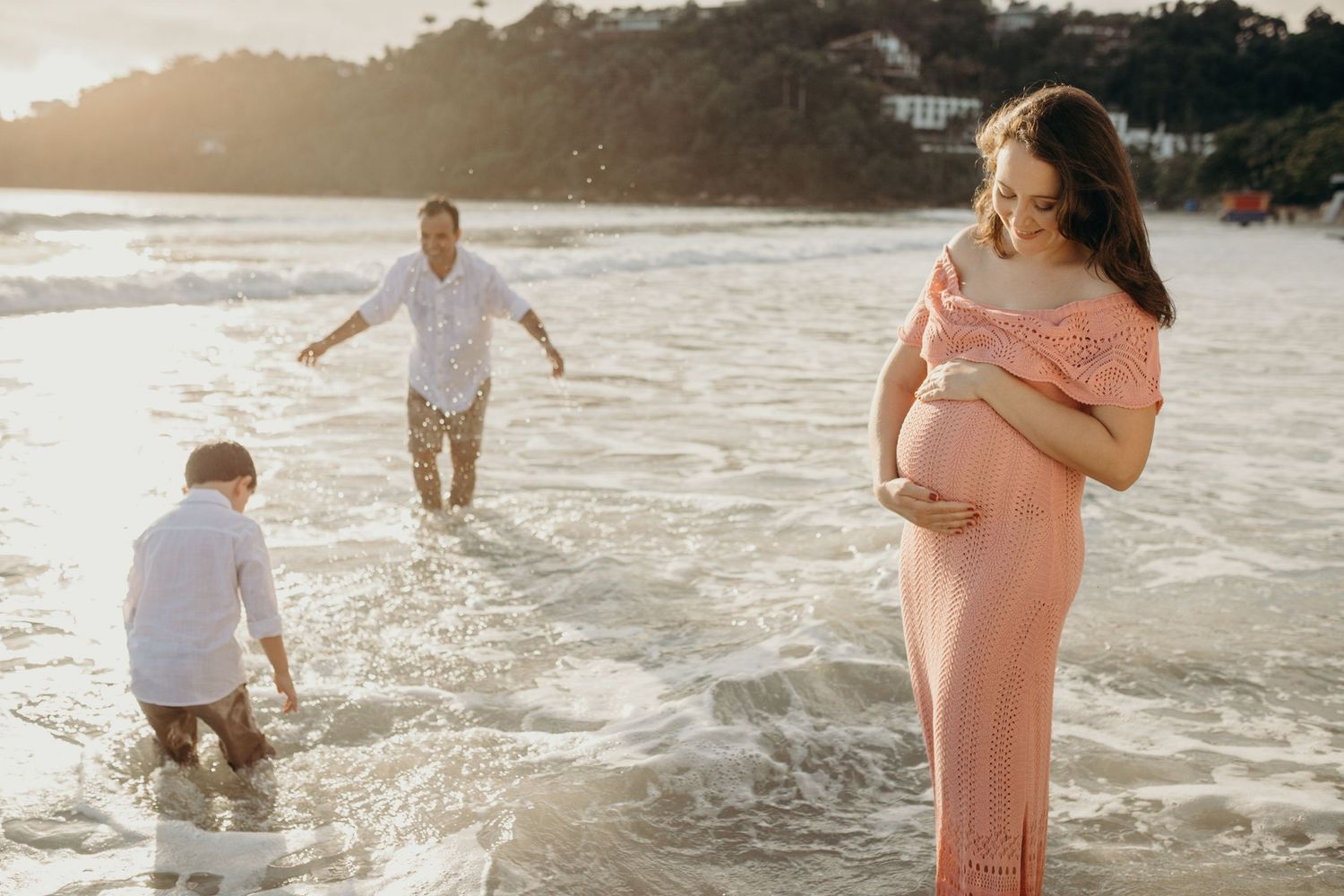 A family enjoying the beach waves at sunset with one wearing a flowing pink dress.