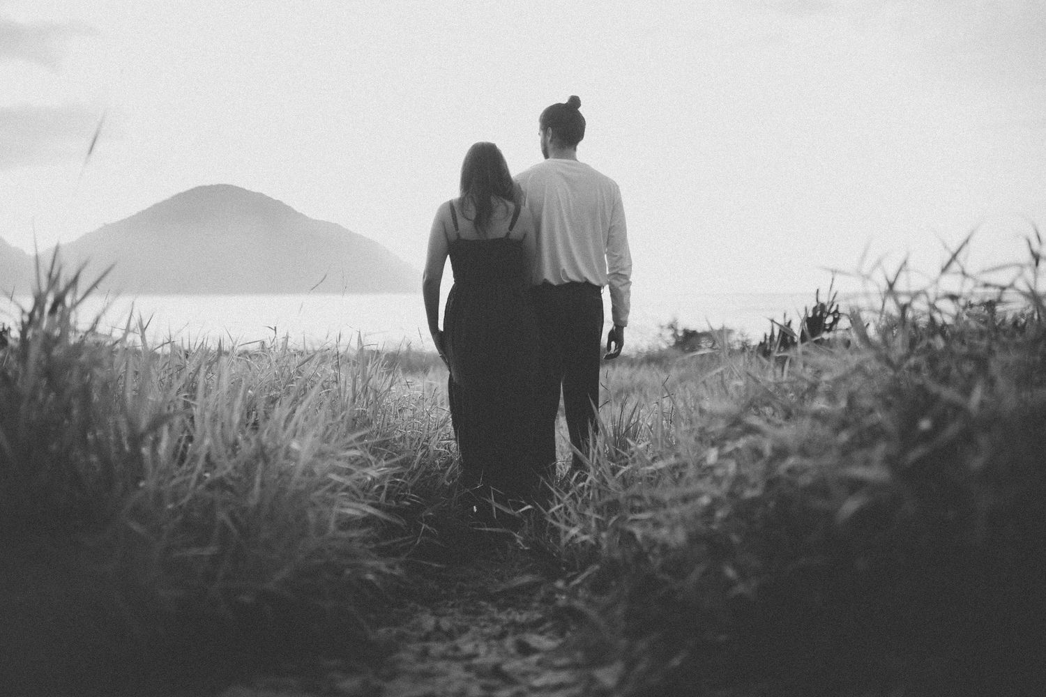 A silhouetted couple walks together on a hilltop path during sunset.