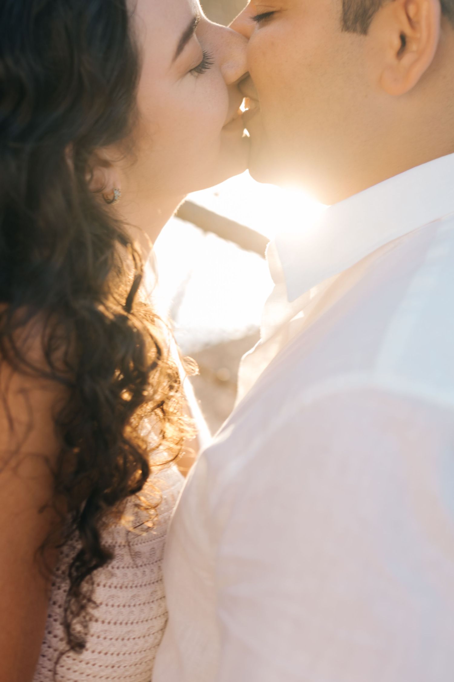 Intimate close-up of a couple kissing with sunlight streaming between them.