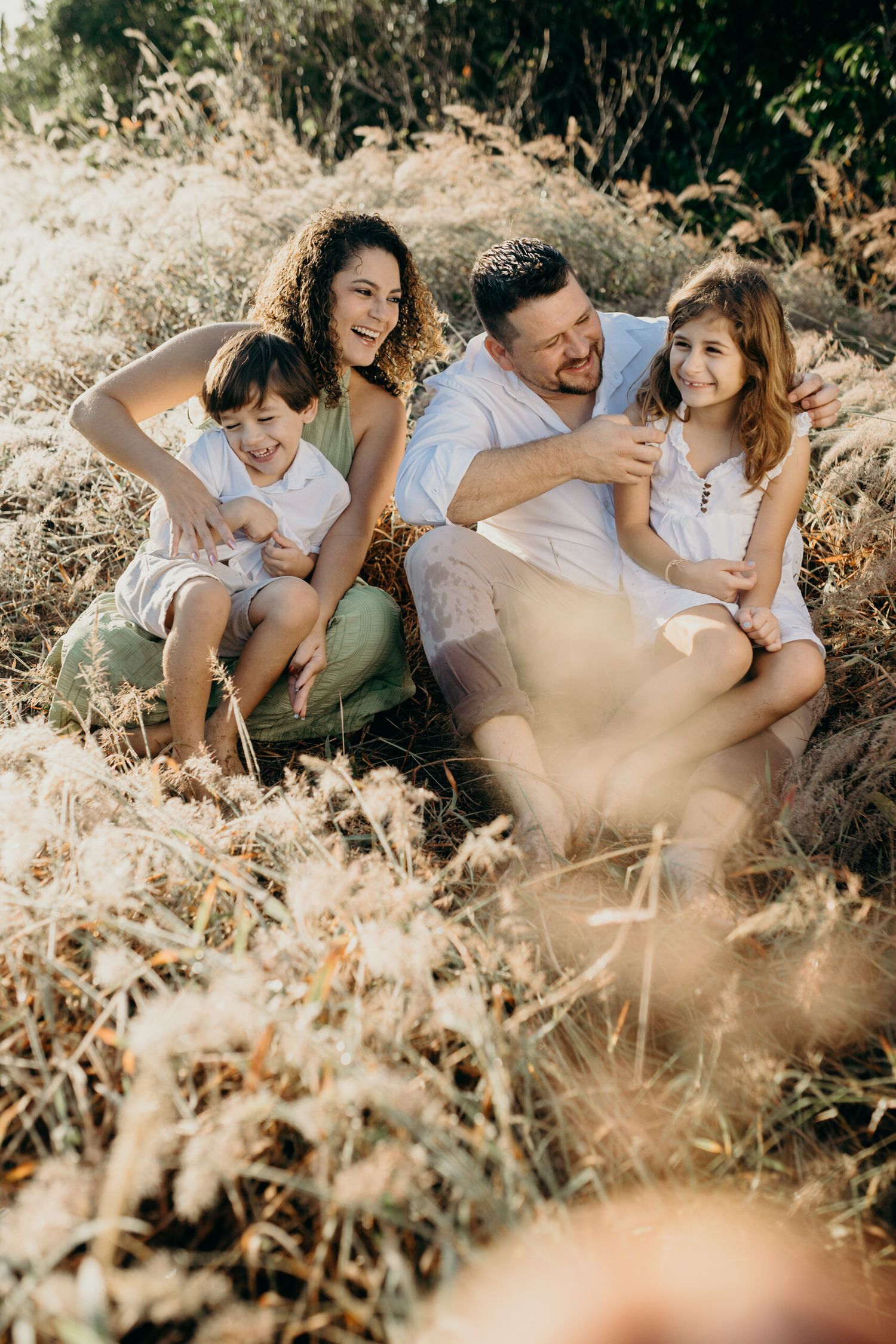 Family enjoying a sunny day together sitting in tall grass during a golden hour photoshoot.