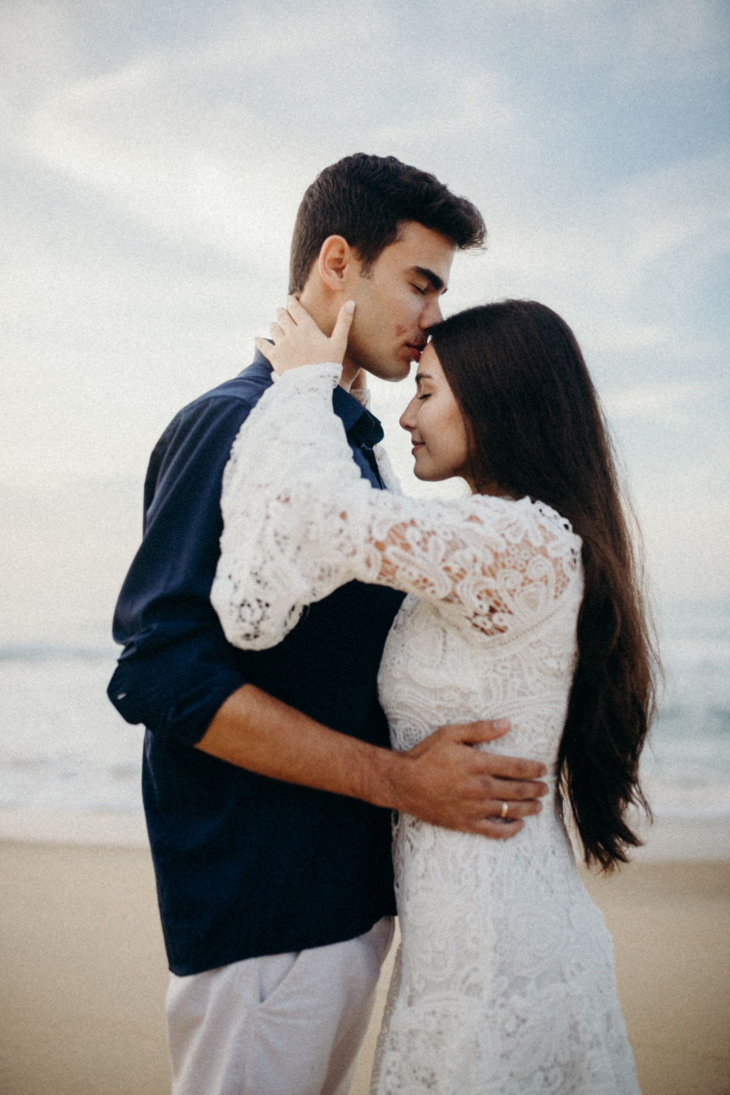 Tender moment between a couple in navy and white as they embrace on a sandy beach.