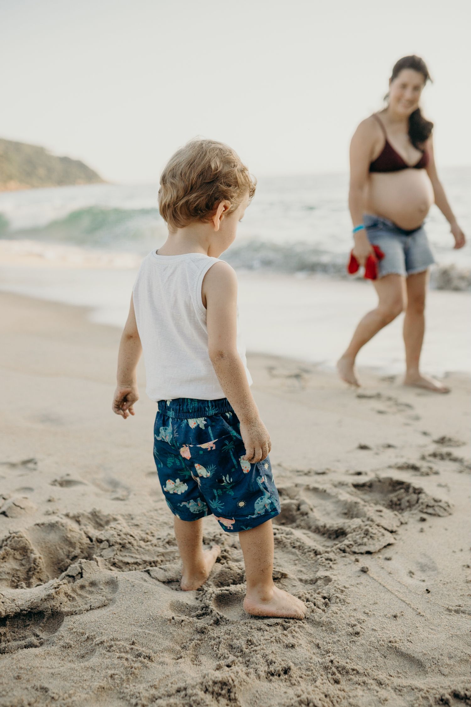 Child exploring sandy beach with family members in the background.