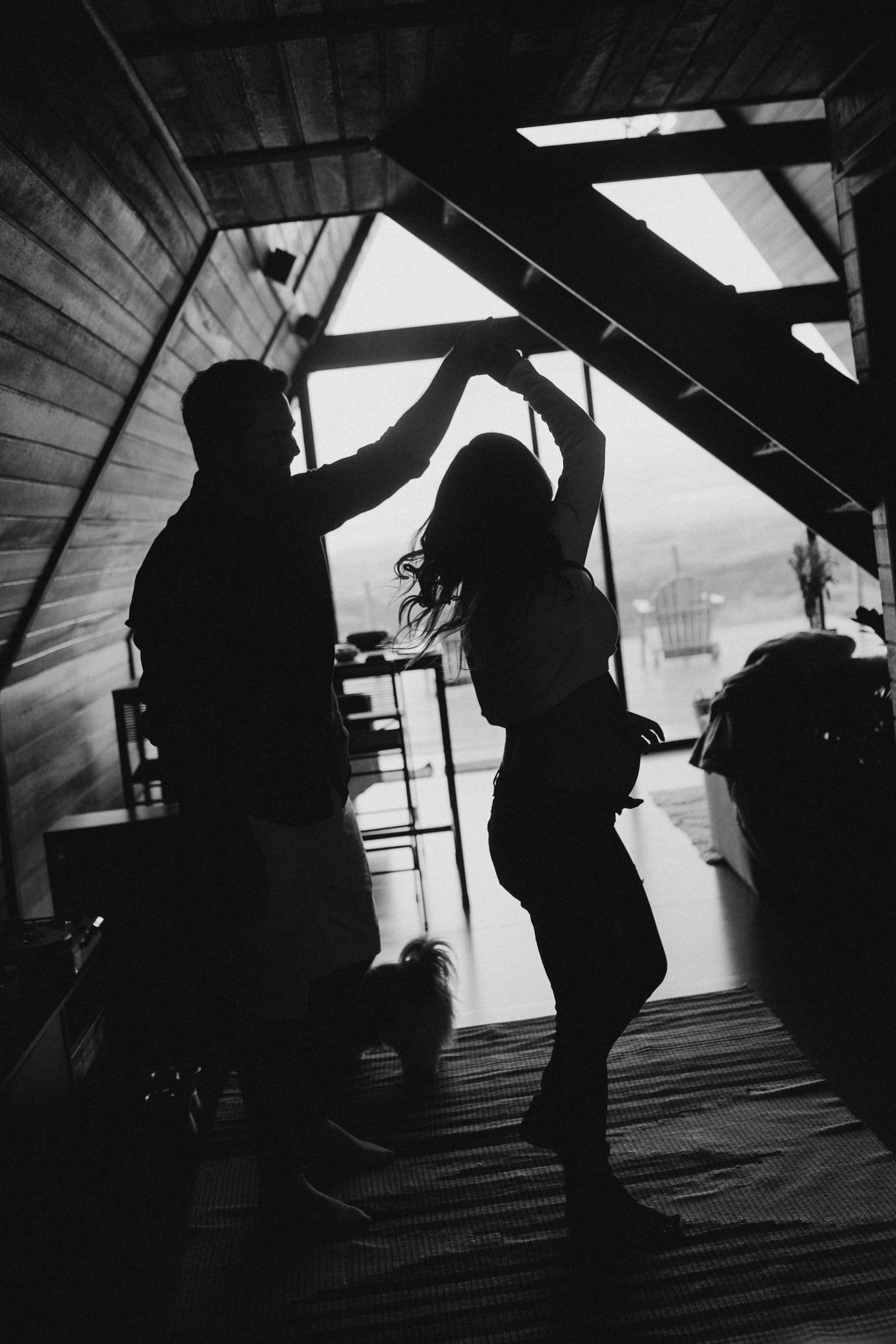 Two silhouettes dance together in a wooden attic space illuminated by natural light.
