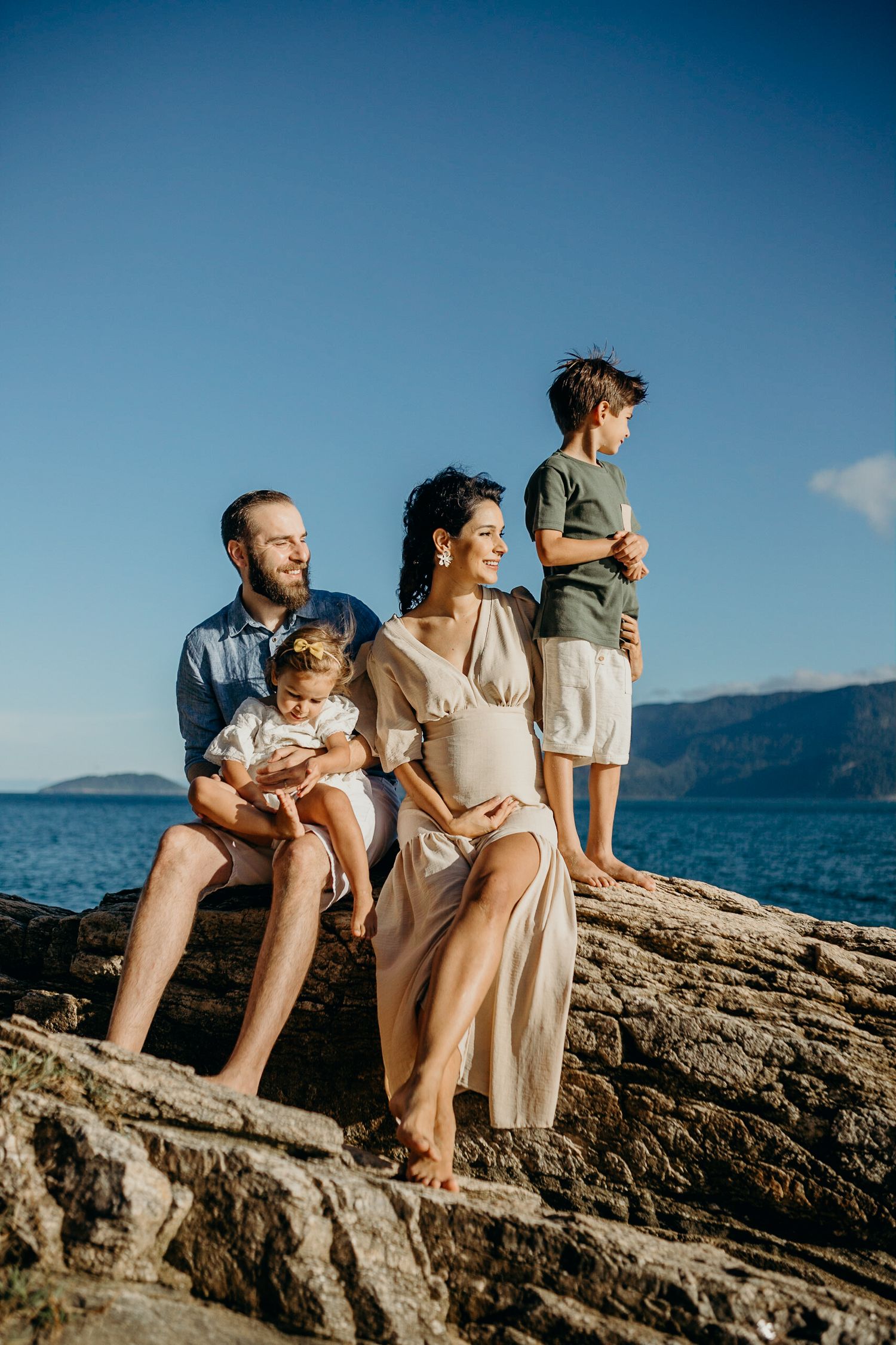 Family sitting together on coastal rocks overlooking the ocean on a bright sunny day.