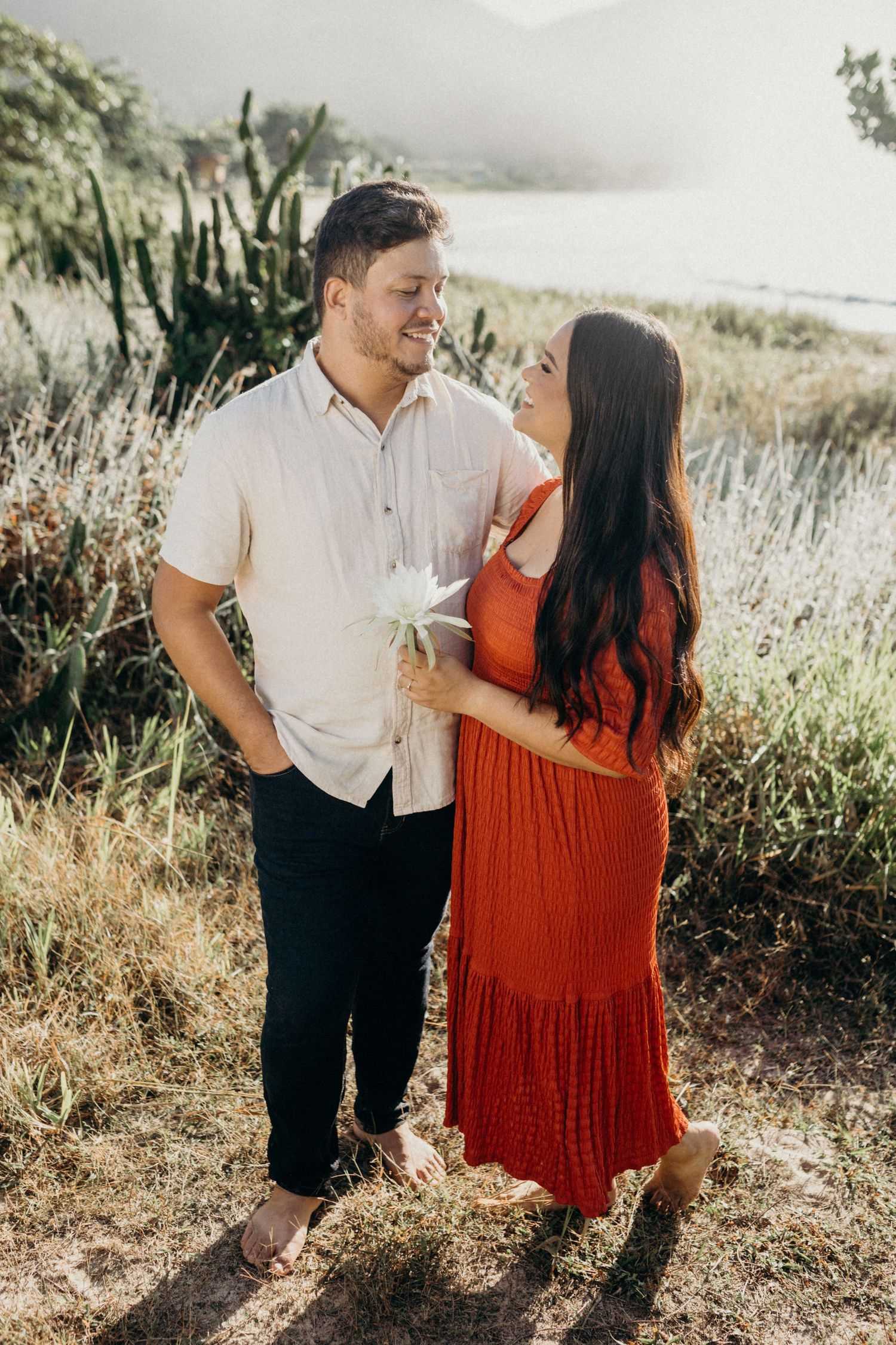 Couple in coordinated outfits smiling at each other on hillside with mountain vista.