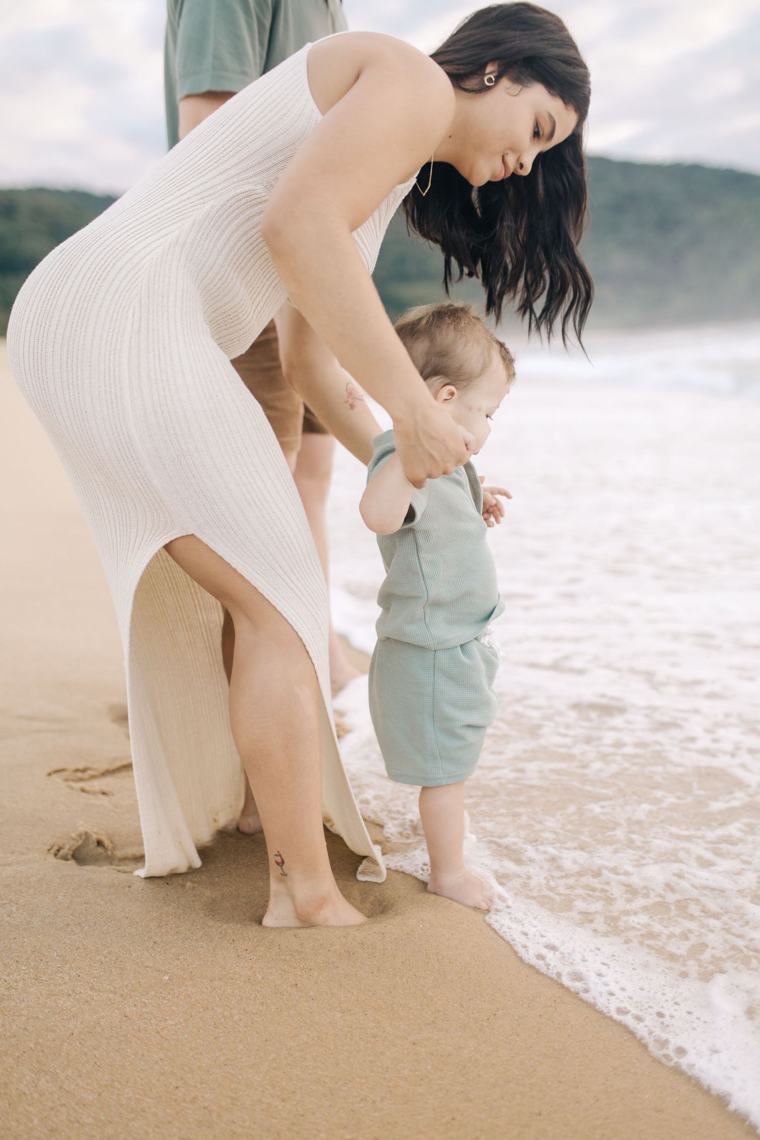 Parent and child explore the shoreline together while playing in gentle beach waves.