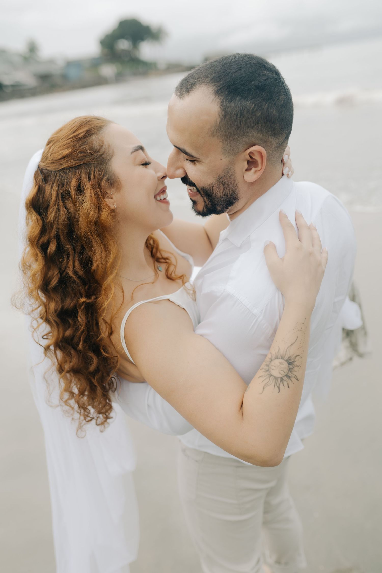 Intimate portrait of laughing couple in white beach wedding attire.