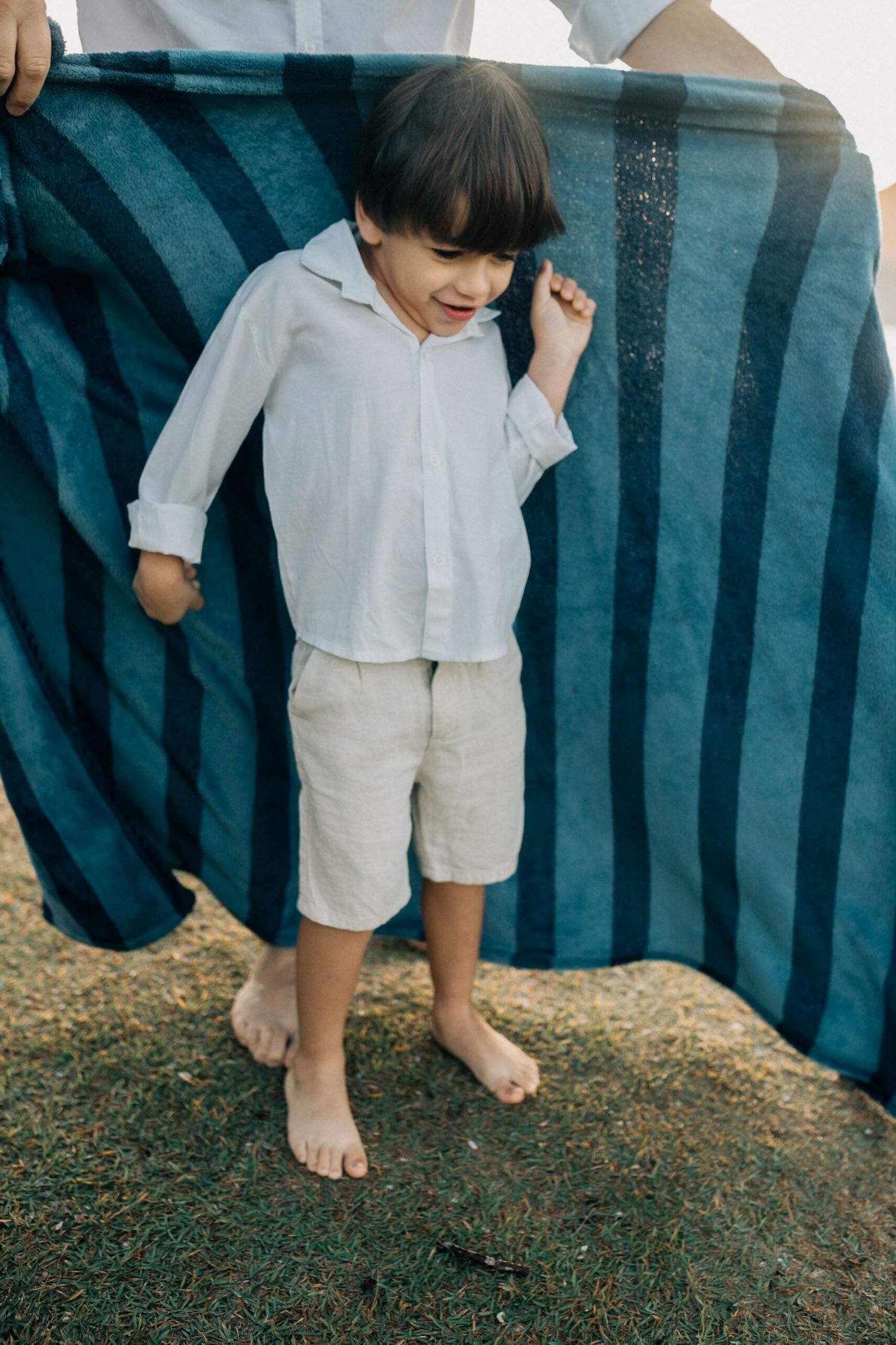 Bare feet and white clothing visible beneath a blue striped beach towel outdoors.