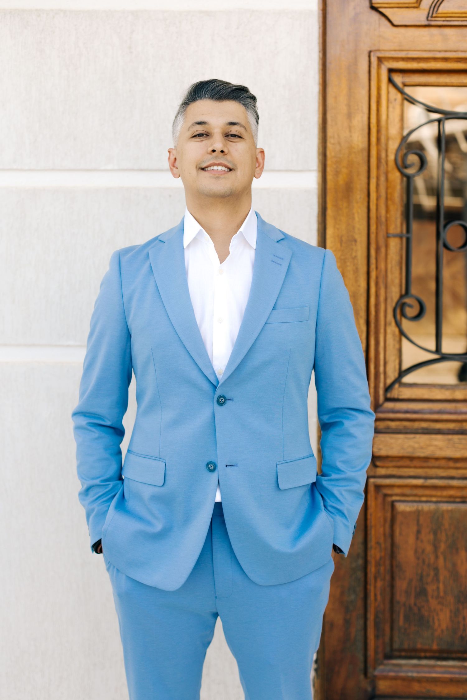 Person wearing bright blue suit standing confidently against white wall and ornate door.