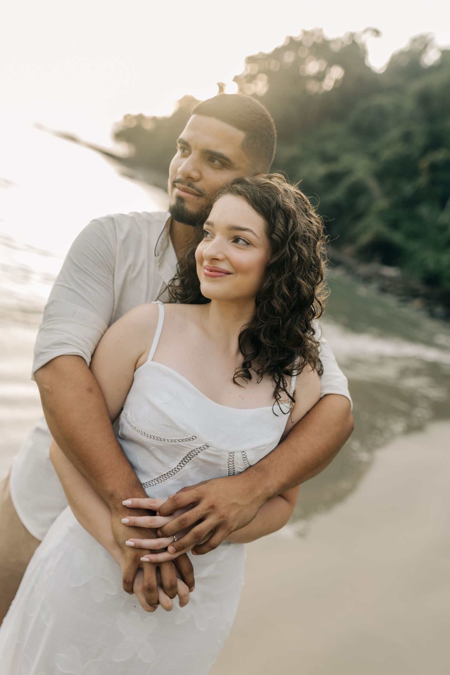 A romantic embrace between a couple wearing white on a scenic beach at golden hour.