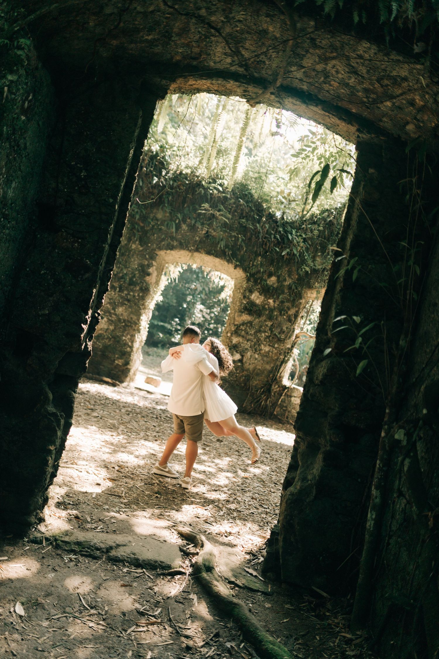 Couple exploring stone archway ruins in dappled sunlight.
