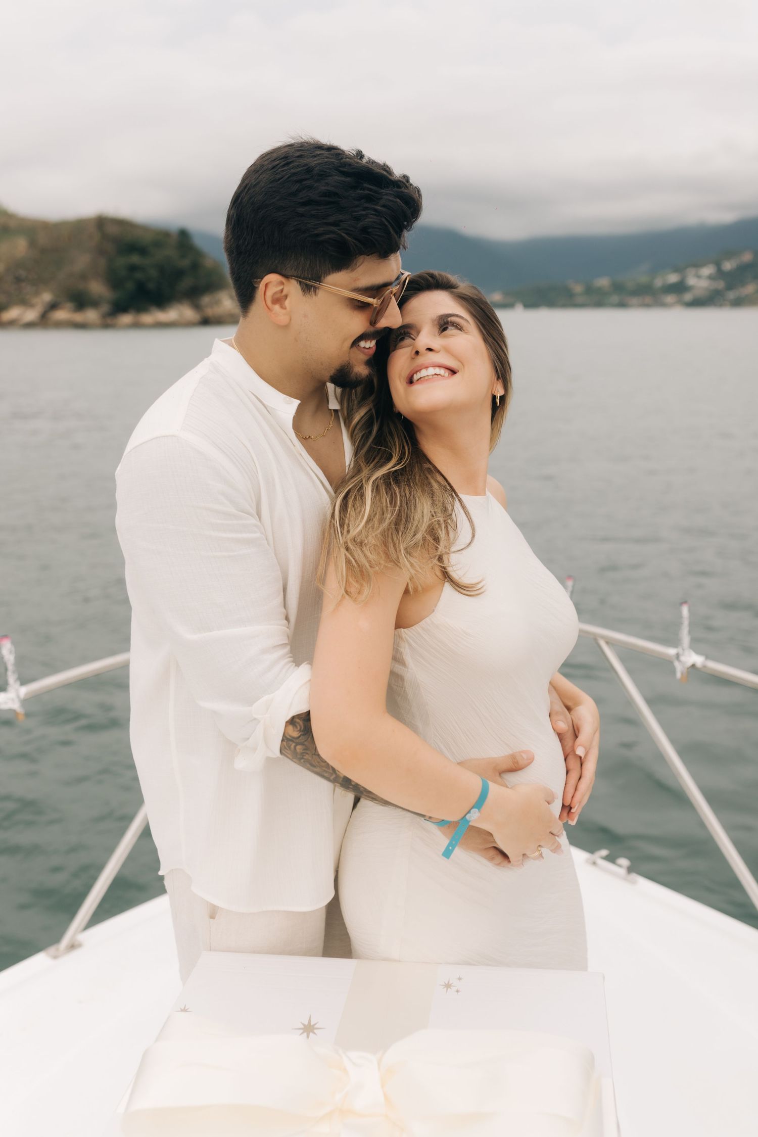 Romantic embrace on yacht bow with mountainous coastline in background.