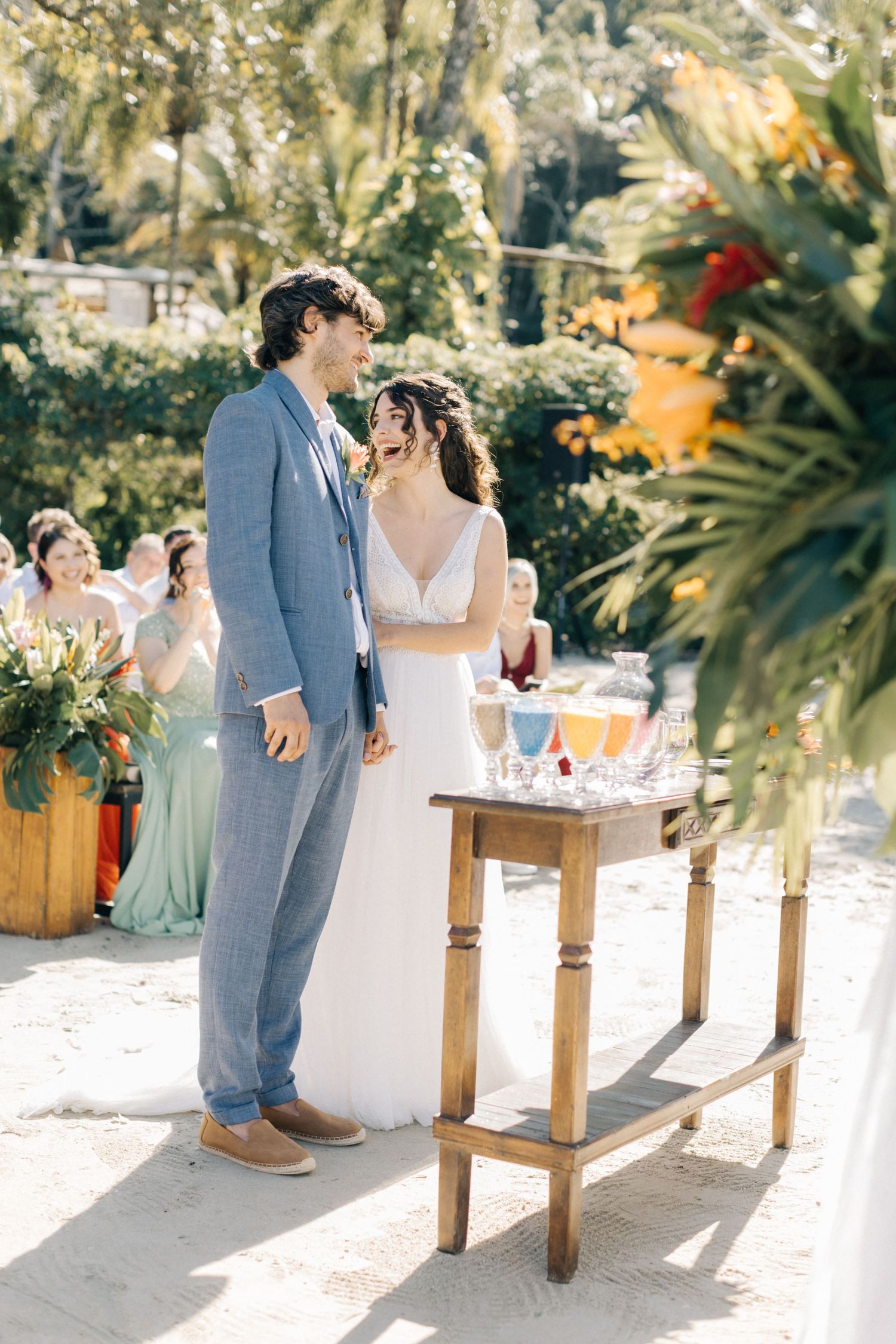 Couple standing by a rustic wooden table at their sunny outdoor wedding reception.