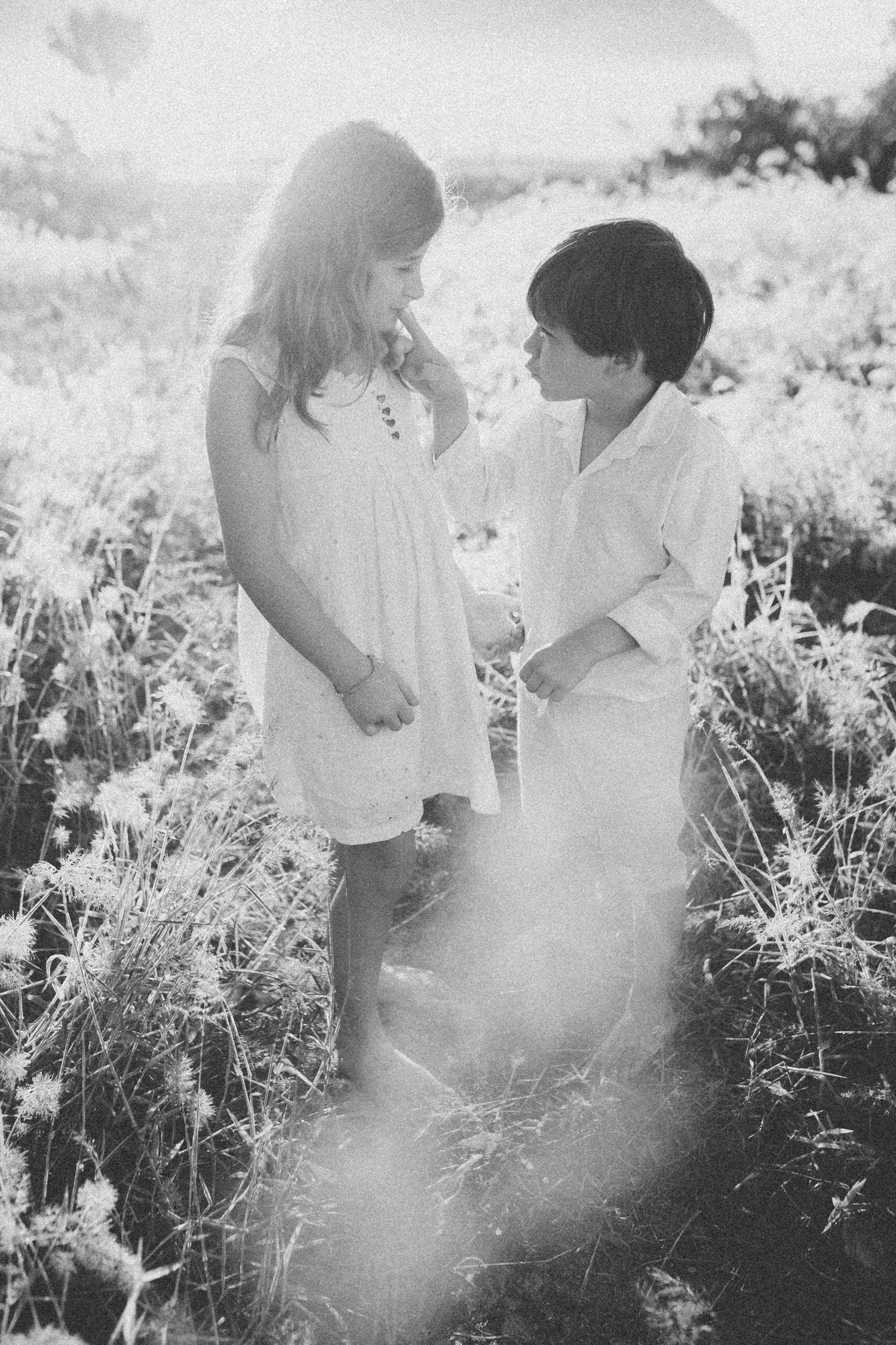 Black and white image of children sharing a tender moment in a field of wild grass.