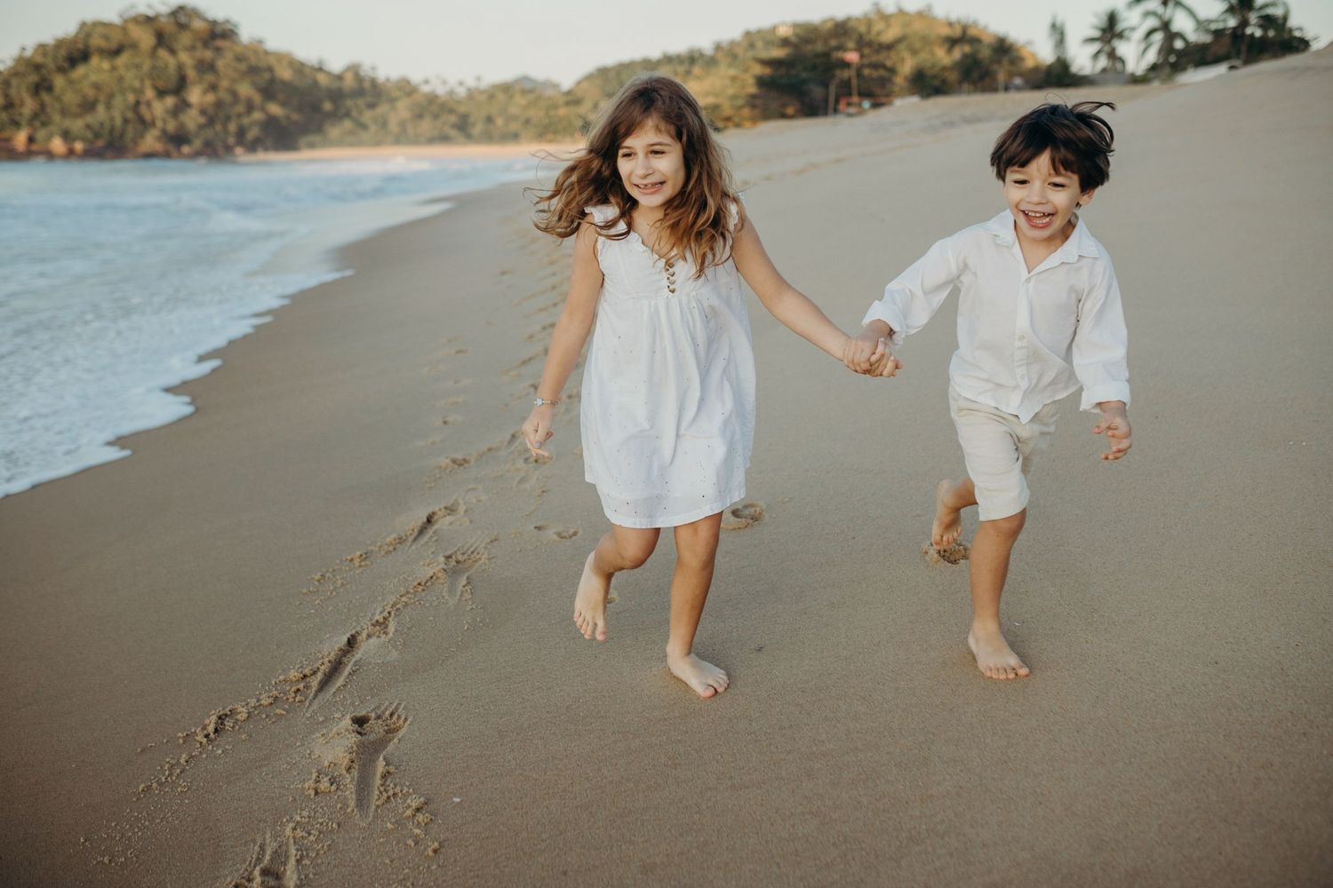 Kids jumping and running freely along a scenic beach at golden hour.