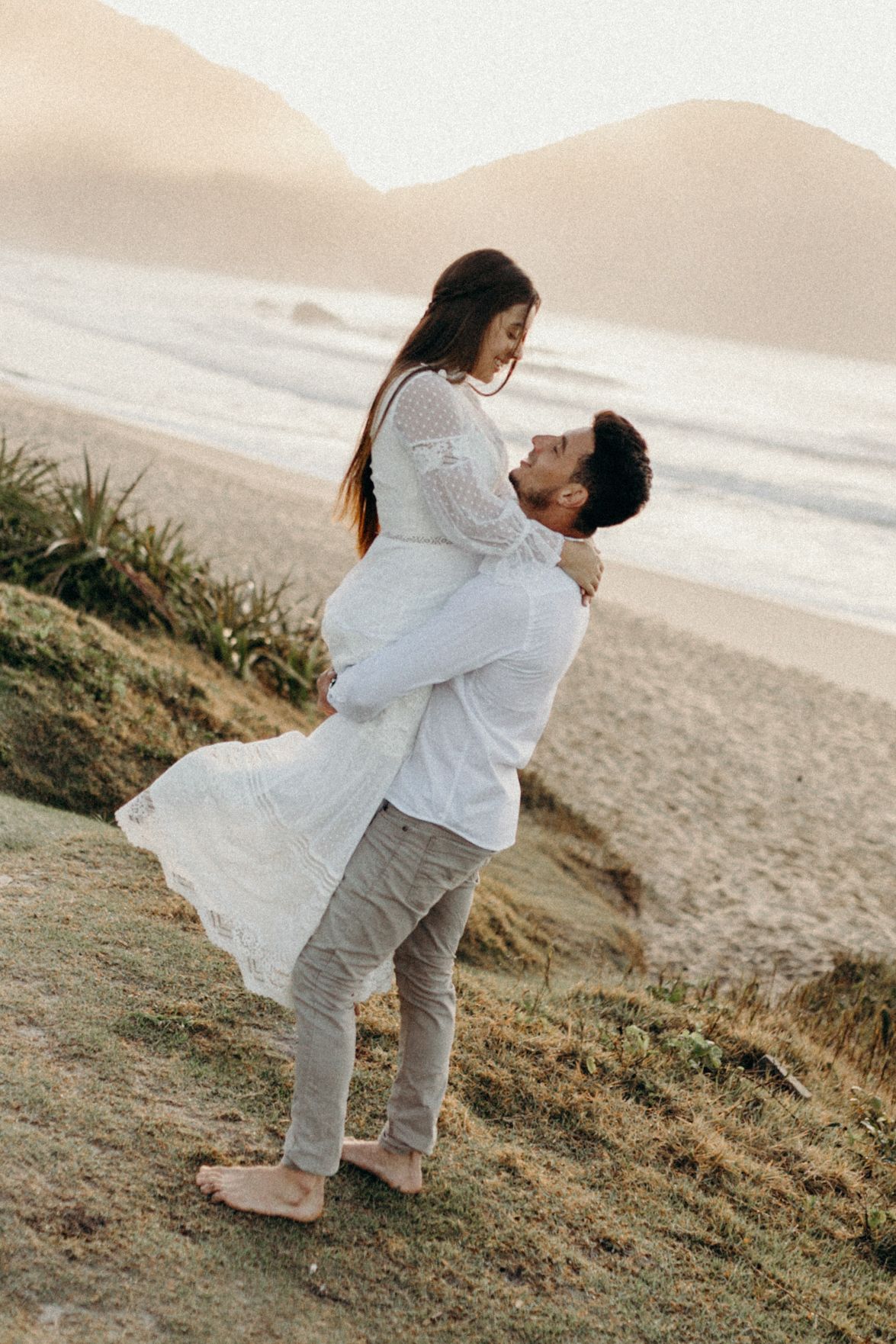 Dancing couple in white outfits share joyful moment on coastal cliff.