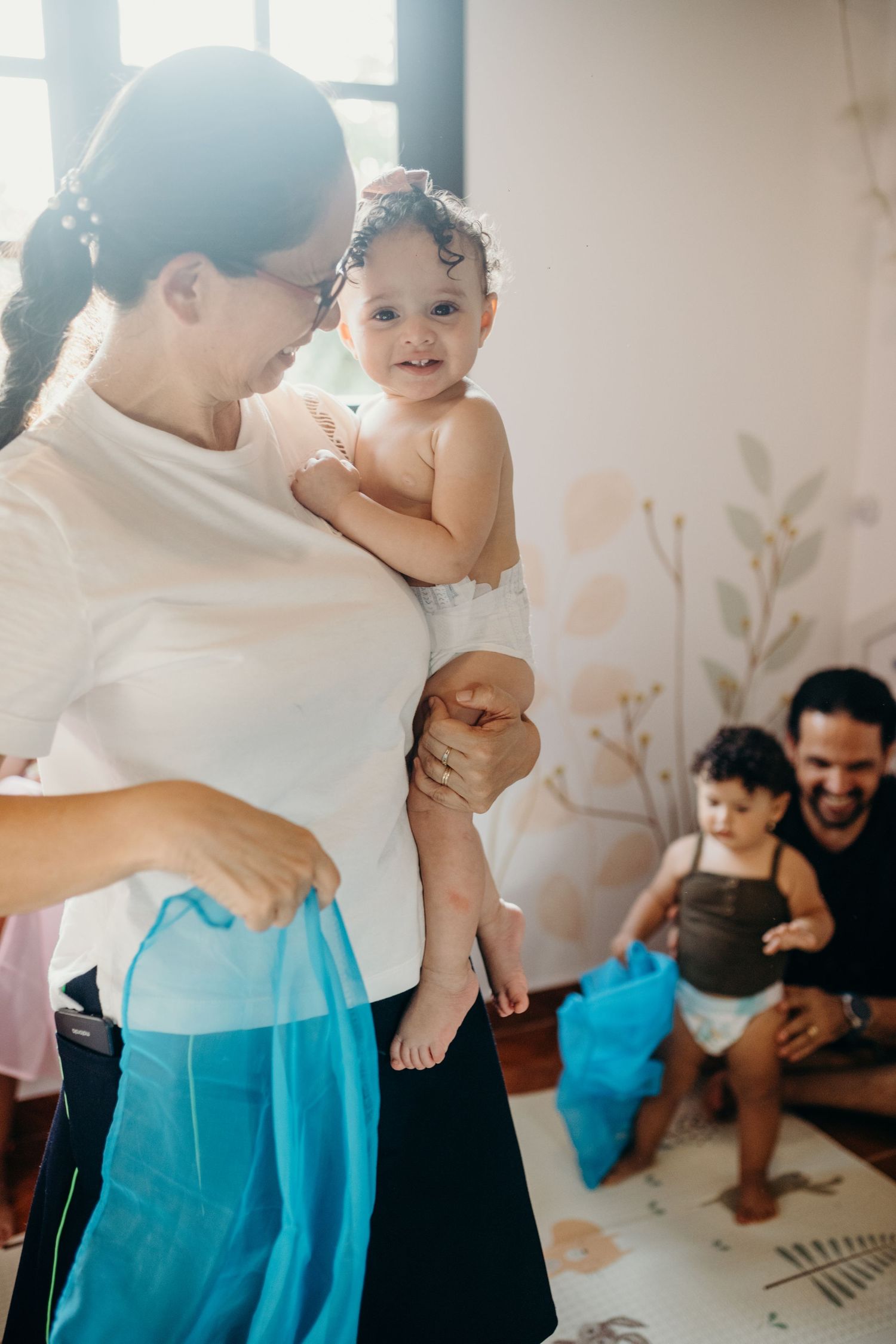 A playful moment at home with a small child in a white shirt and blue pants being held up.