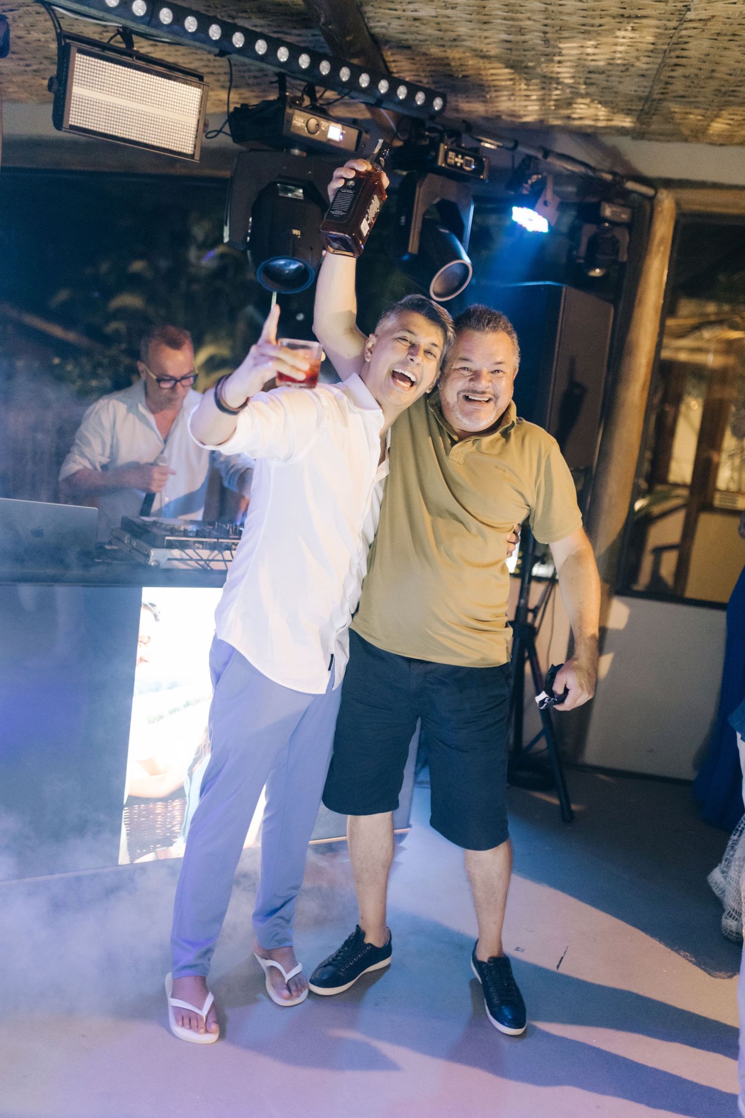 Wedding reception dance party with DJ booth and guests celebrating on foggy dance floor.
