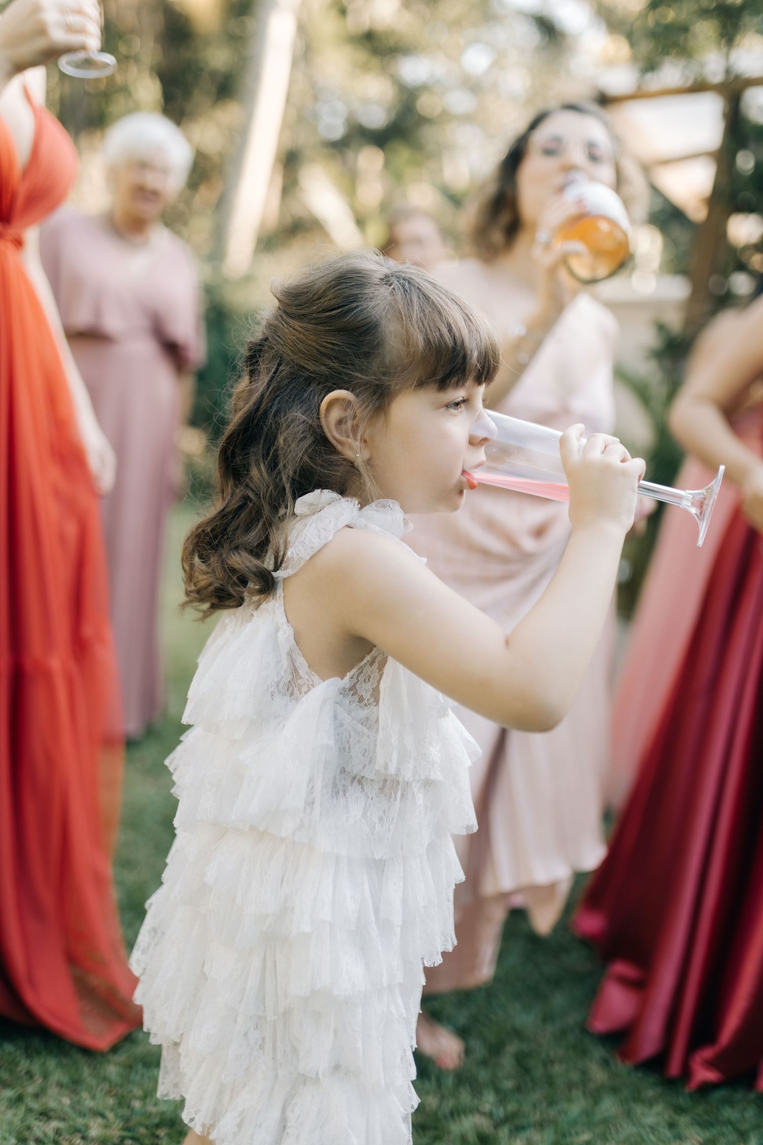 Young flower girl in white lace dress twirls at an outdoor wedding celebration.