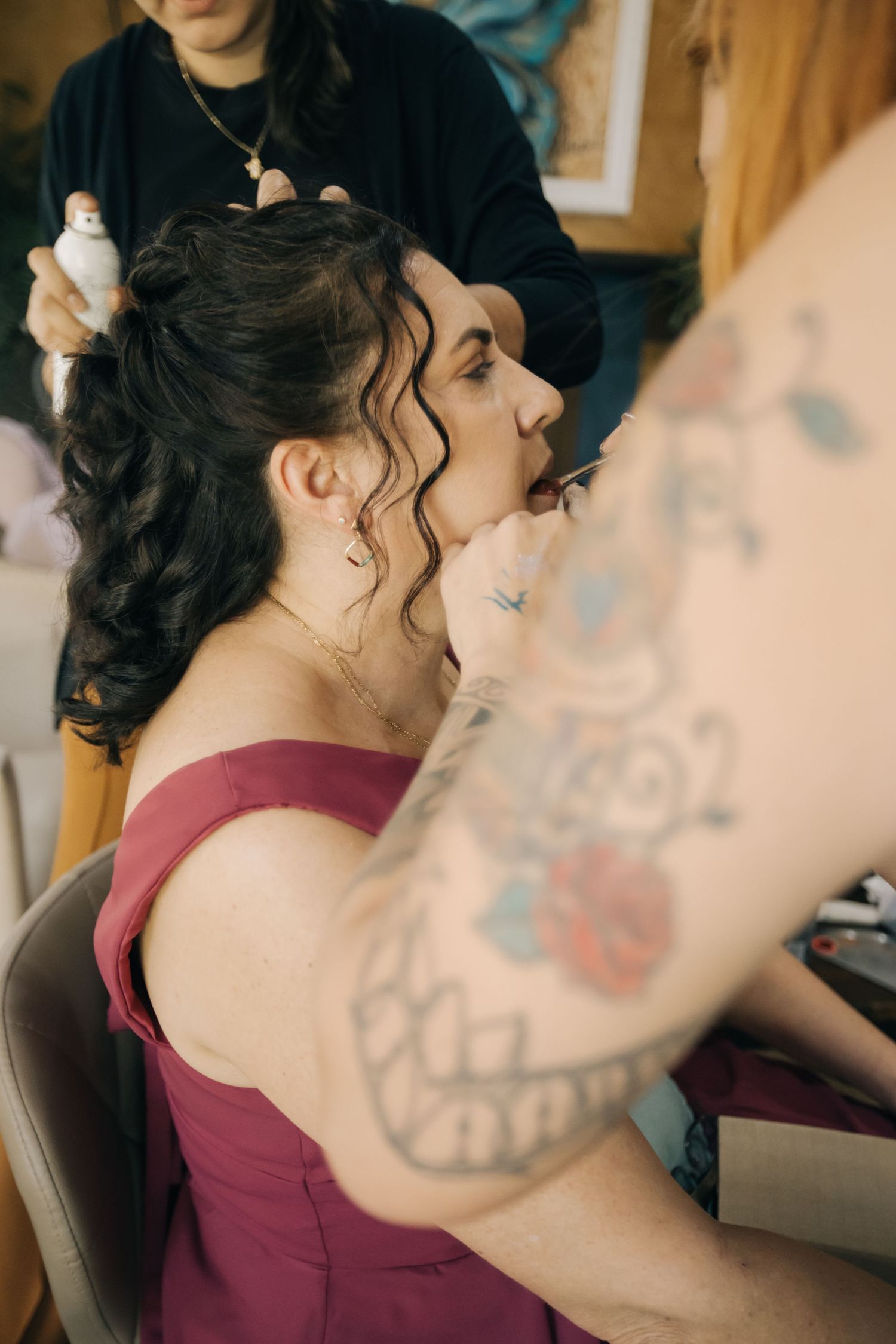 Wedding preparation scene showing hairstyling in progress with burgundy dress.