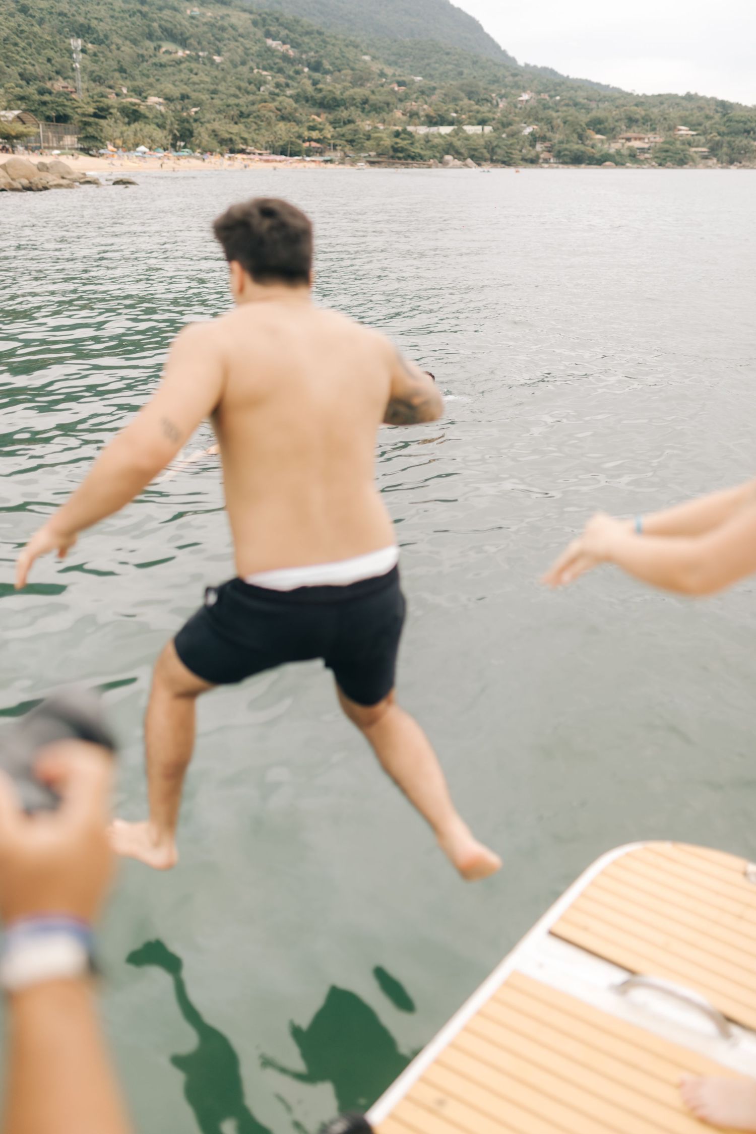 Action sequence of people jumping off wooden boat platform into blue water.