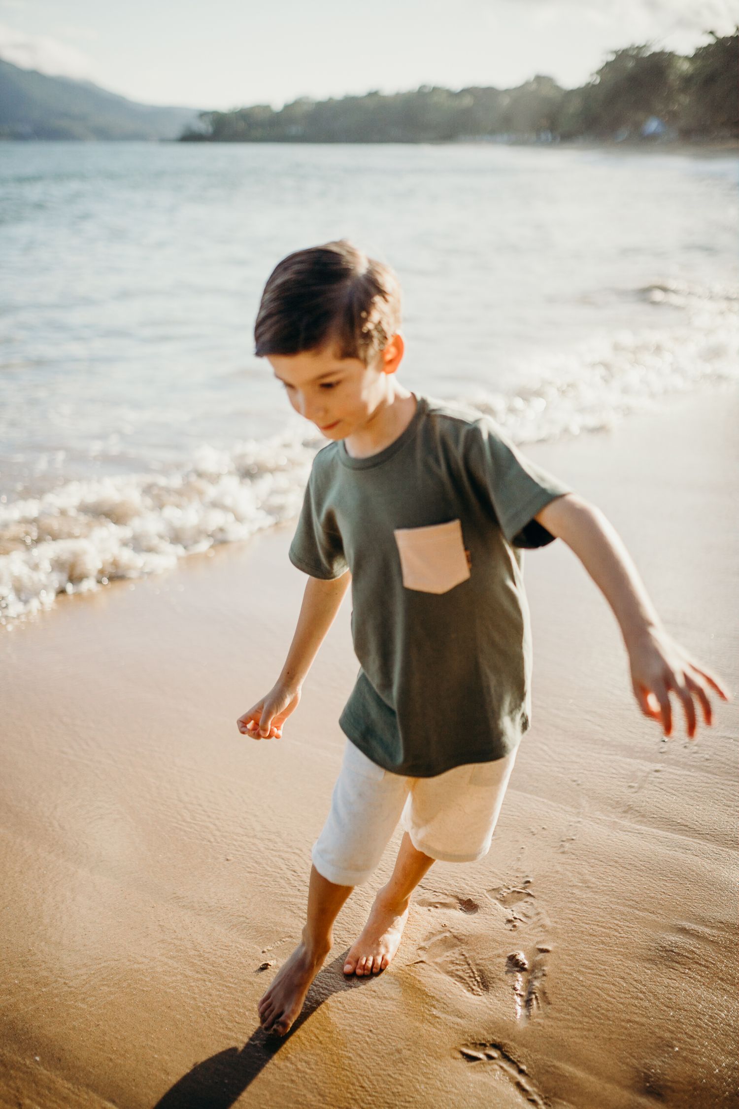 Young child playing on beach shoreline in grey t-shirt during sunset.