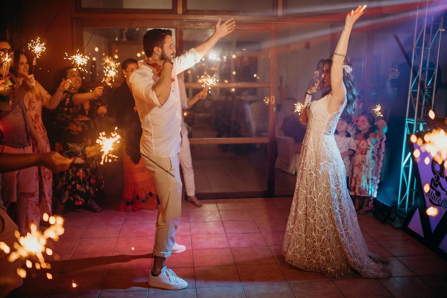 Dancing and celebration beneath sparklers and colorful lights at an evening wedding reception.