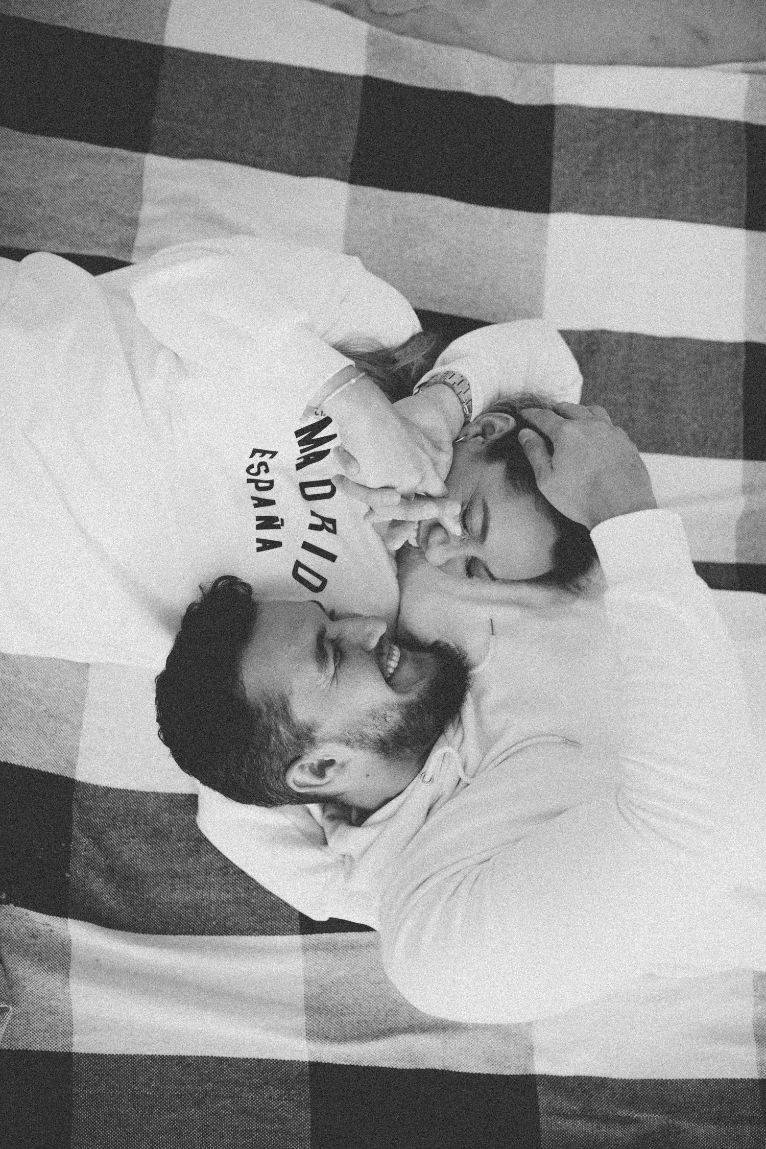 Black and white image of couple lying close together on checkered blanket.