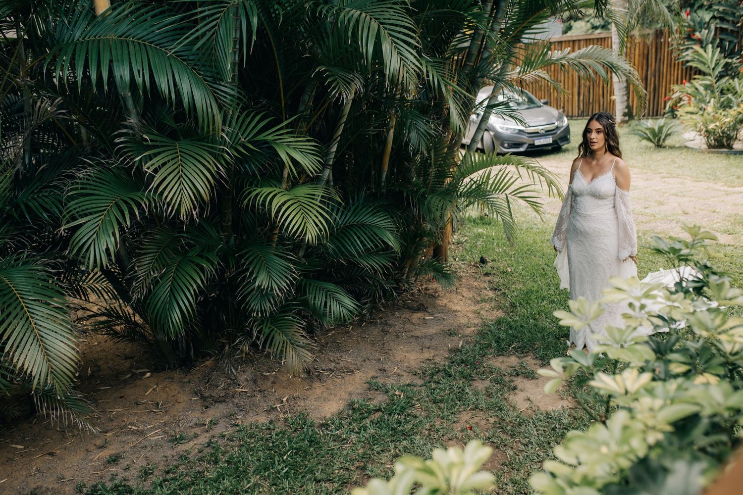 A bride walks through a tropical garden path surrounded by palm trees and greenery.
