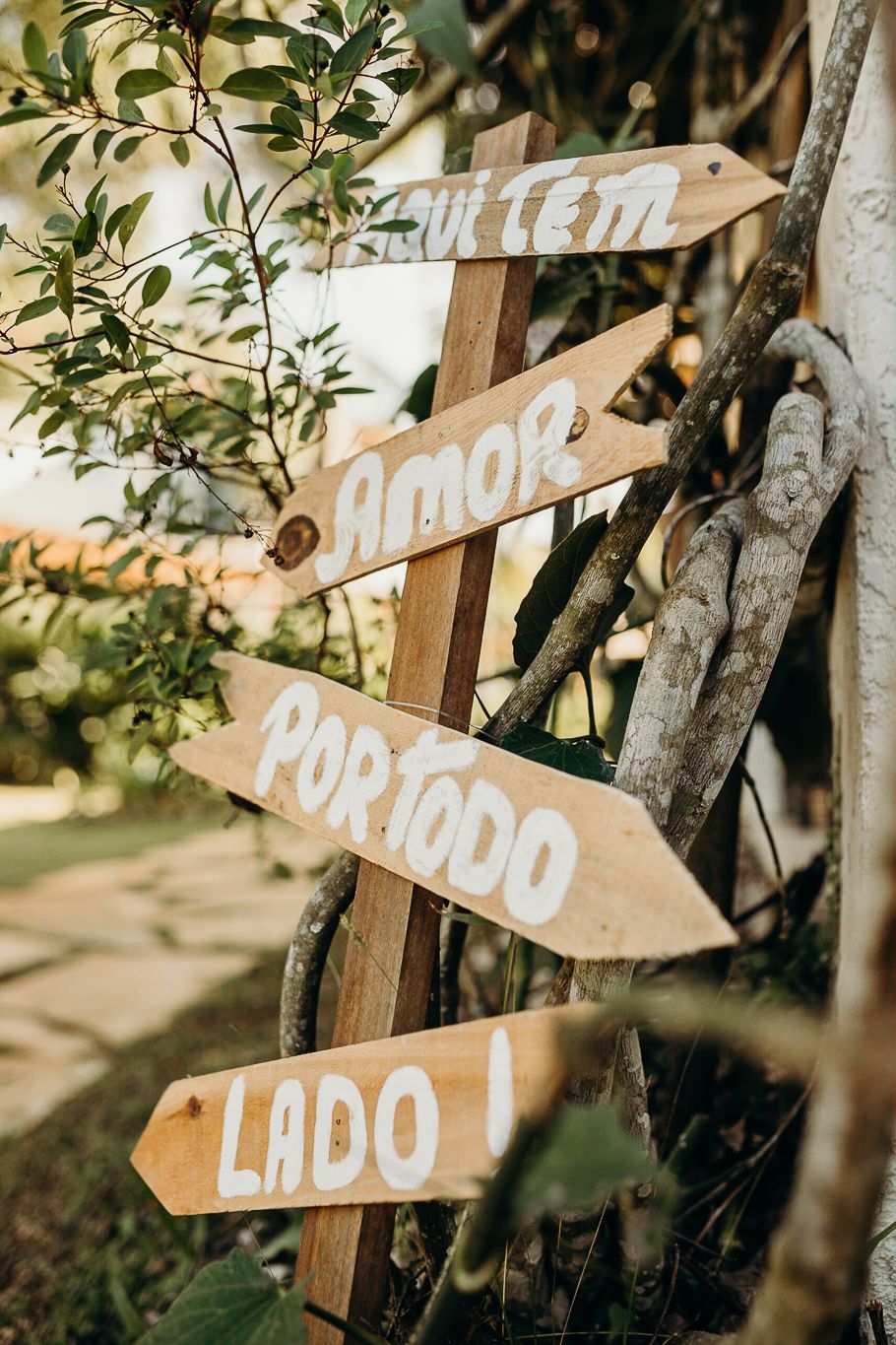 Rustic wooden directional signs mounted on tree branches point to different areas of an outdoor venue.