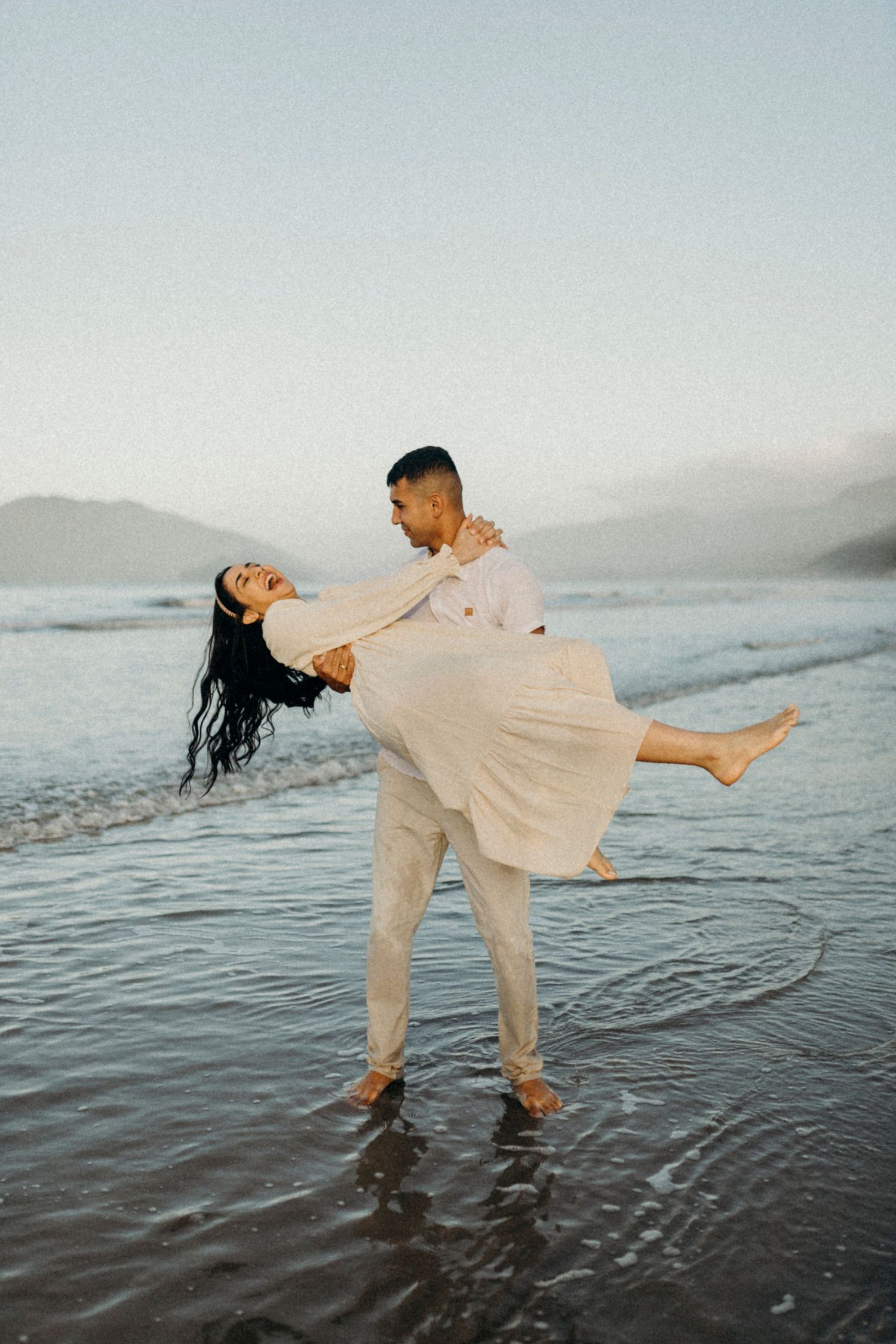Couple dances playfully in shallow water on beach at sunset.