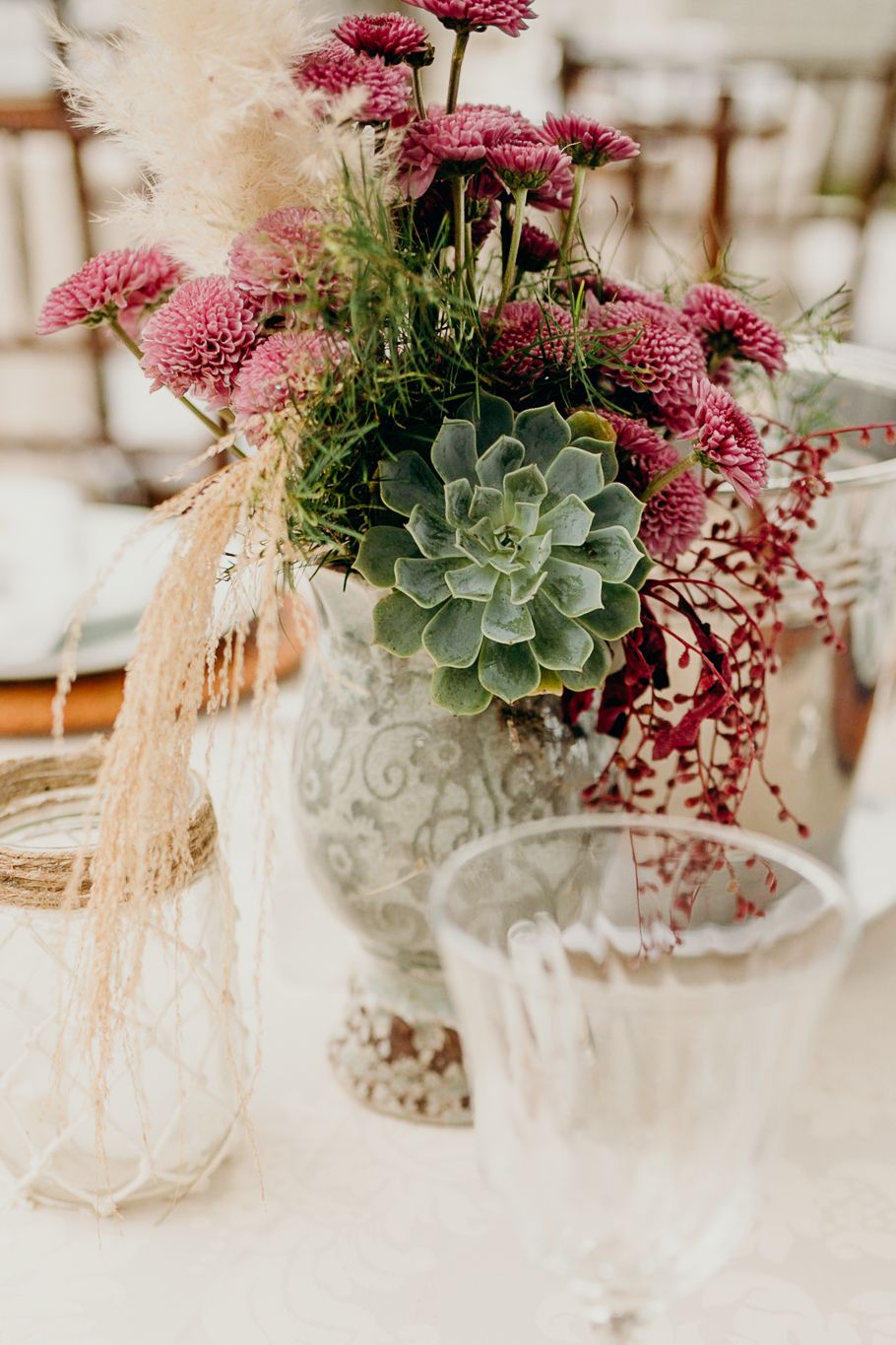 Romantic centerpiece with pink flowers, succulents, and dried pampas grass on white tablecloth.
