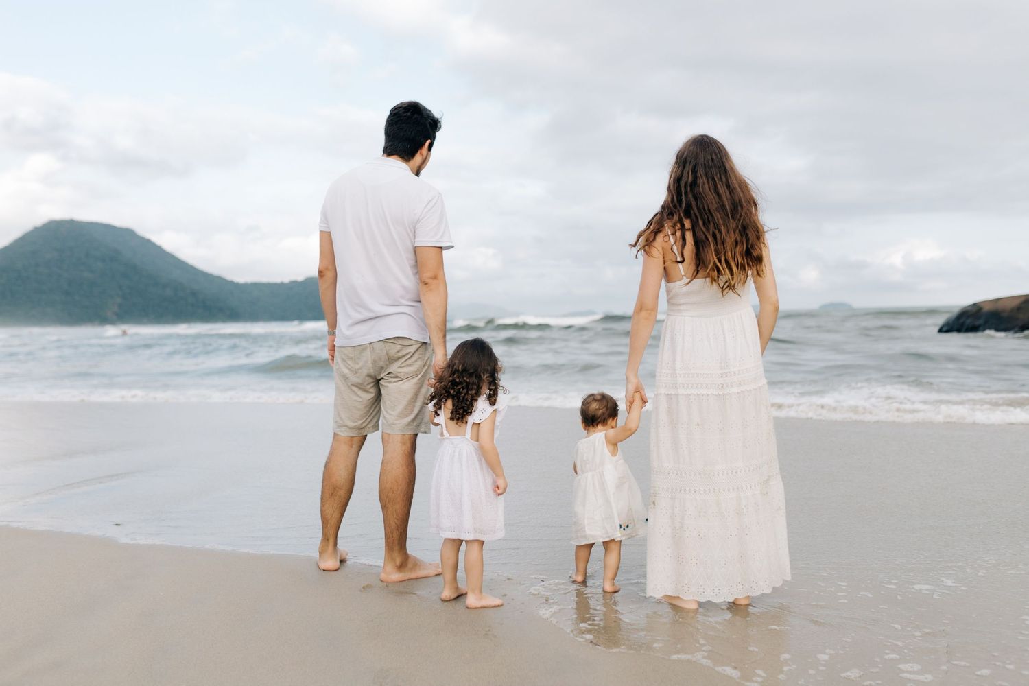 A family in white outfits walking together along a scenic beach.