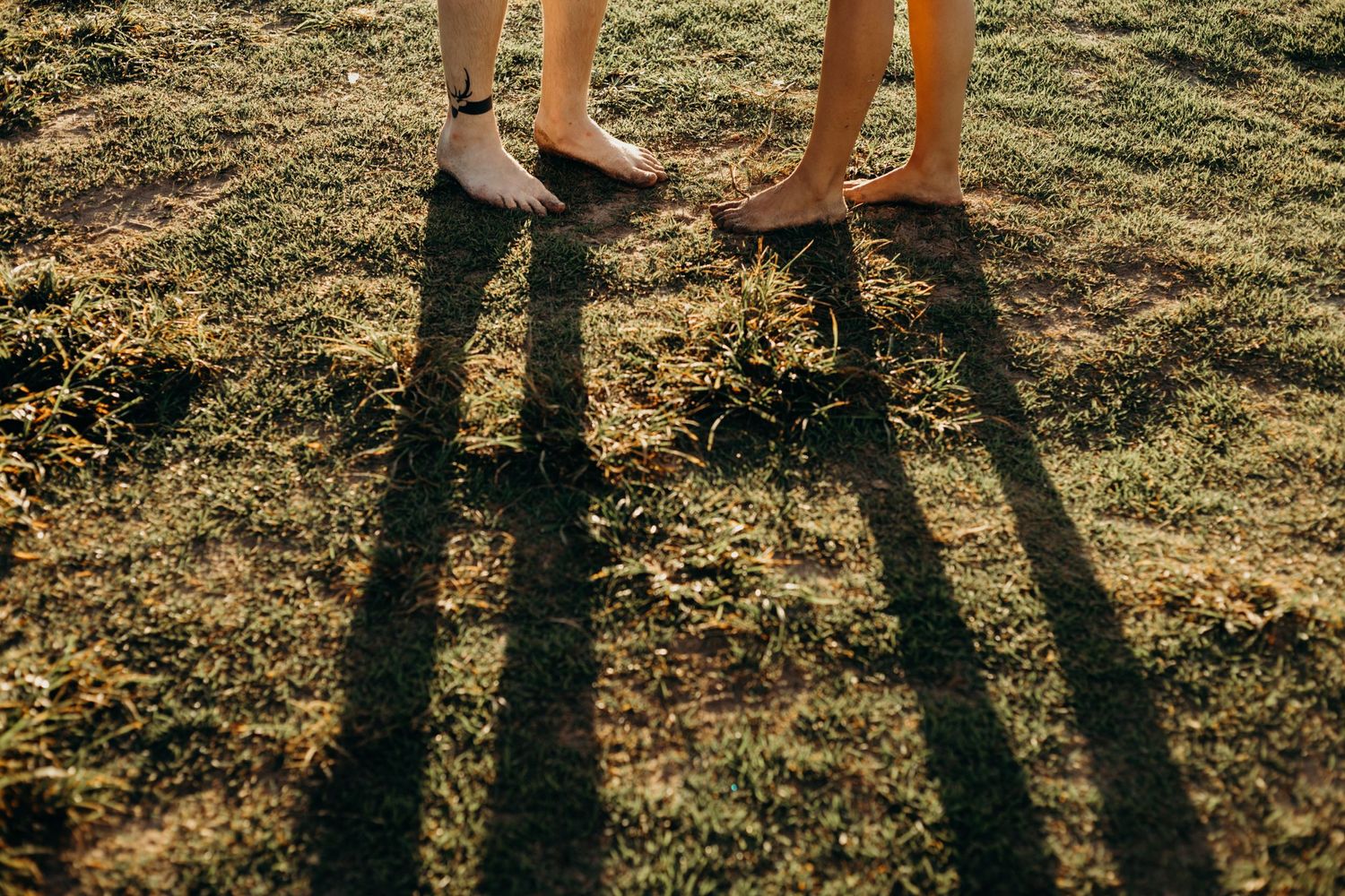 Close-up of feet and long shadows on grass during golden hour.
