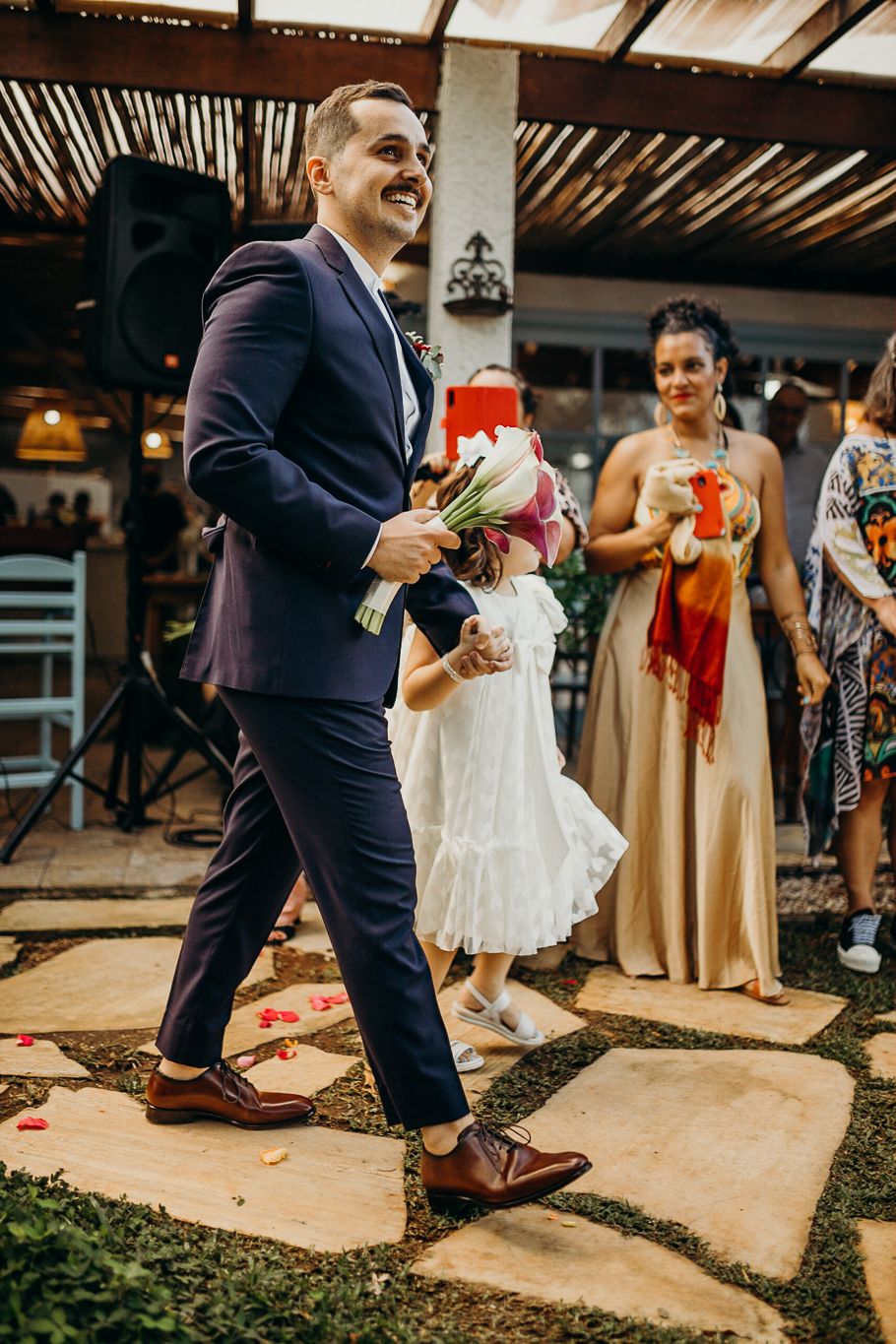 People celebrate on a stone patio under wooden beams during an outdoor wedding reception.