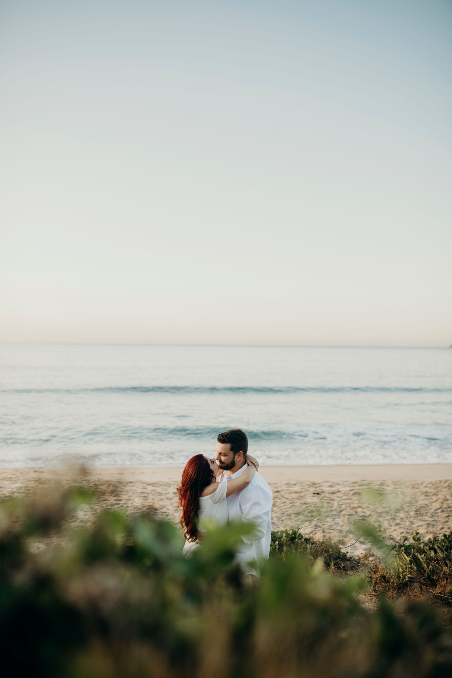 A romantic couple moment captured through beach foliage during sunset.