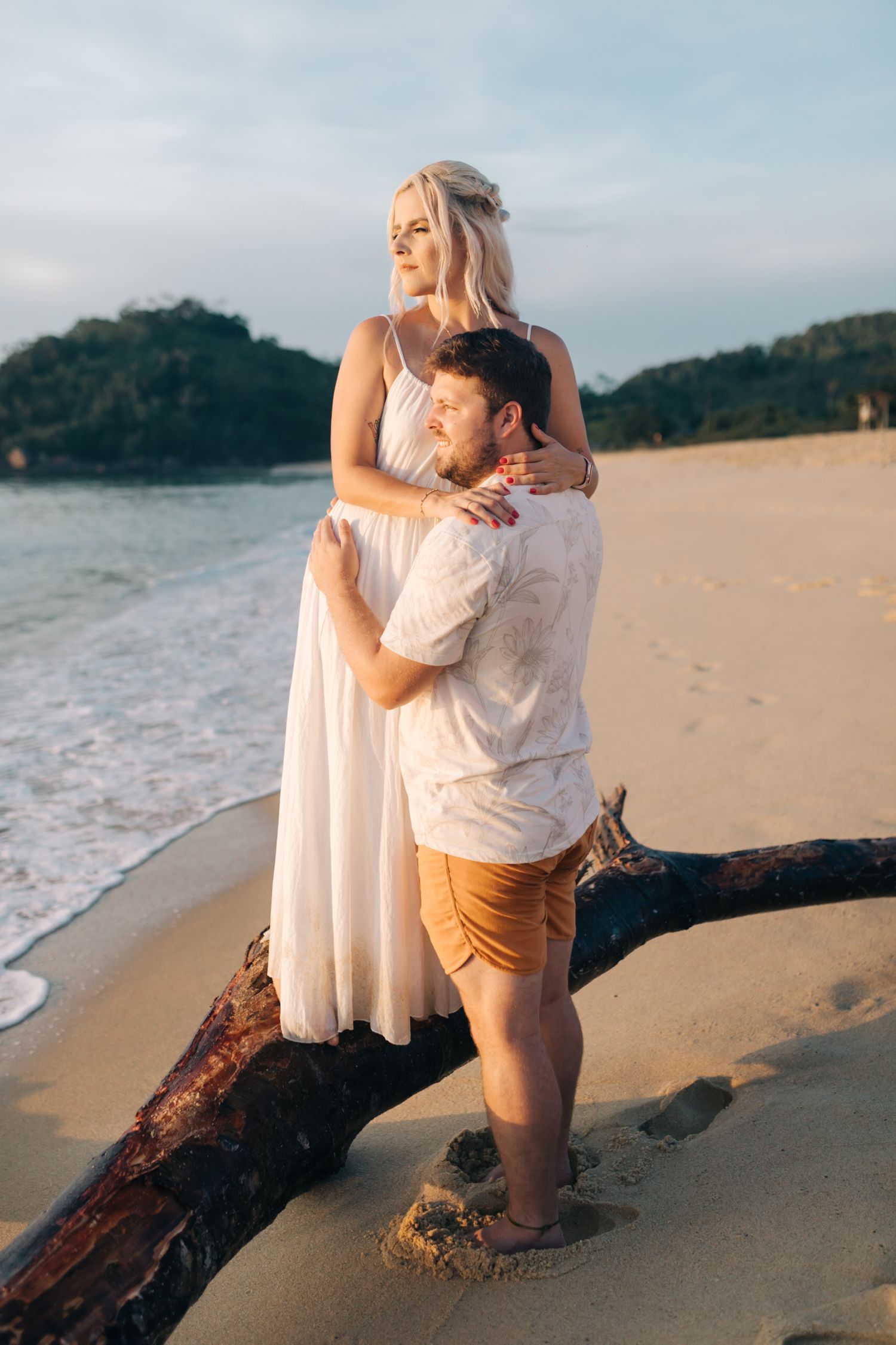 Two people share a playful moment on driftwood at a scenic beach.
