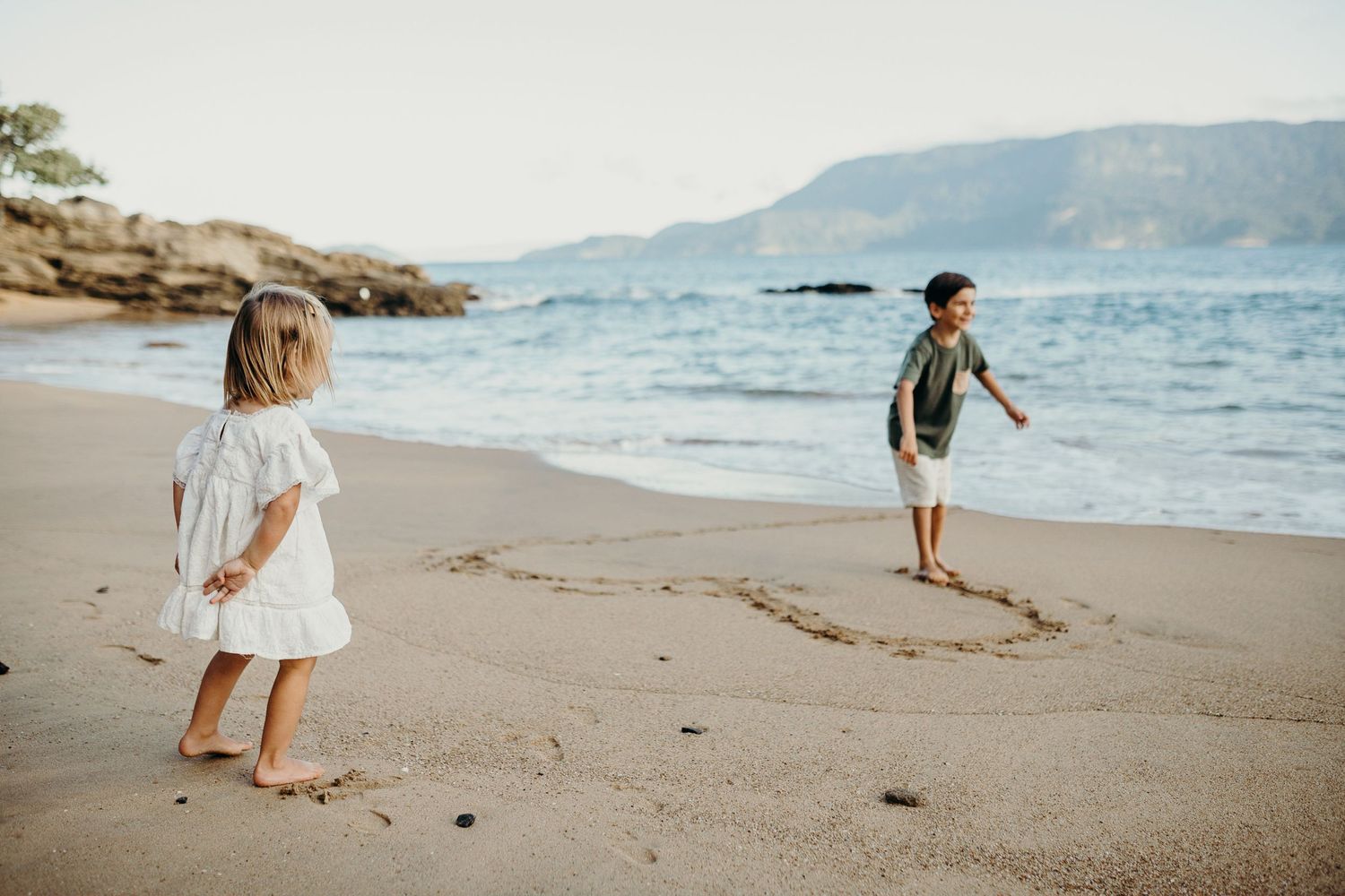 People walking and playing on a scenic beach with mountains in the distance.