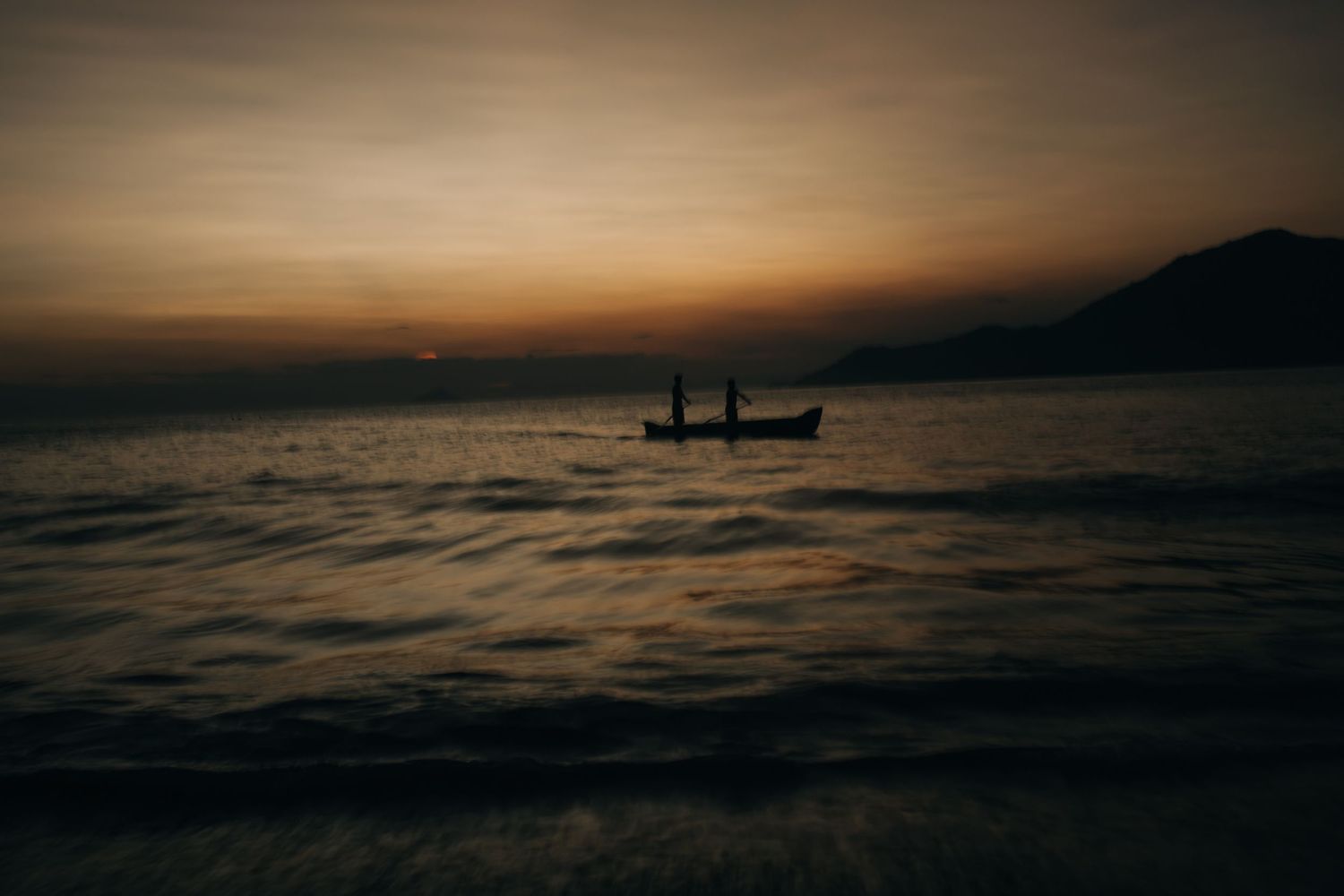 Dark silhouette of fishing boat floating on rippled ocean waters at dusk.
