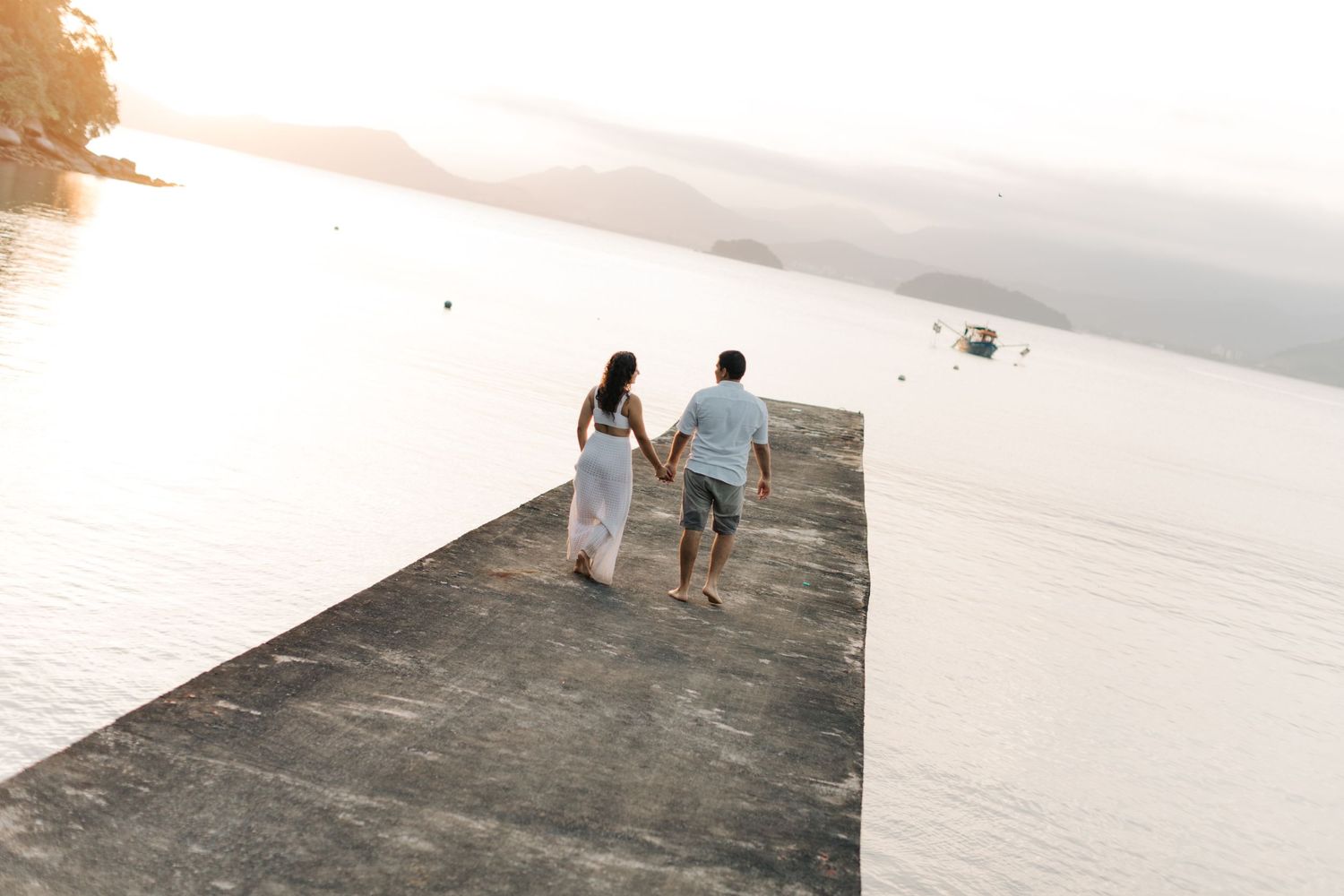 Couple walking together on a concrete pier during sunset.