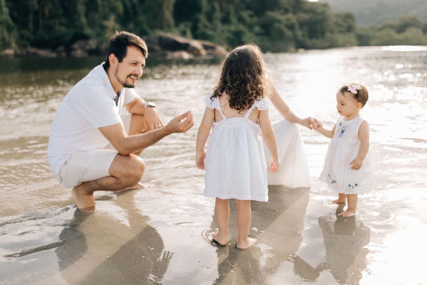 Family playing together in shallow water at beach wearing coordinated white outfits.