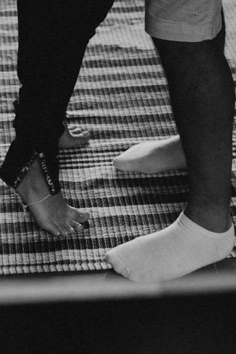 Black and white photo of two pairs of feet standing close together on a striped rug.