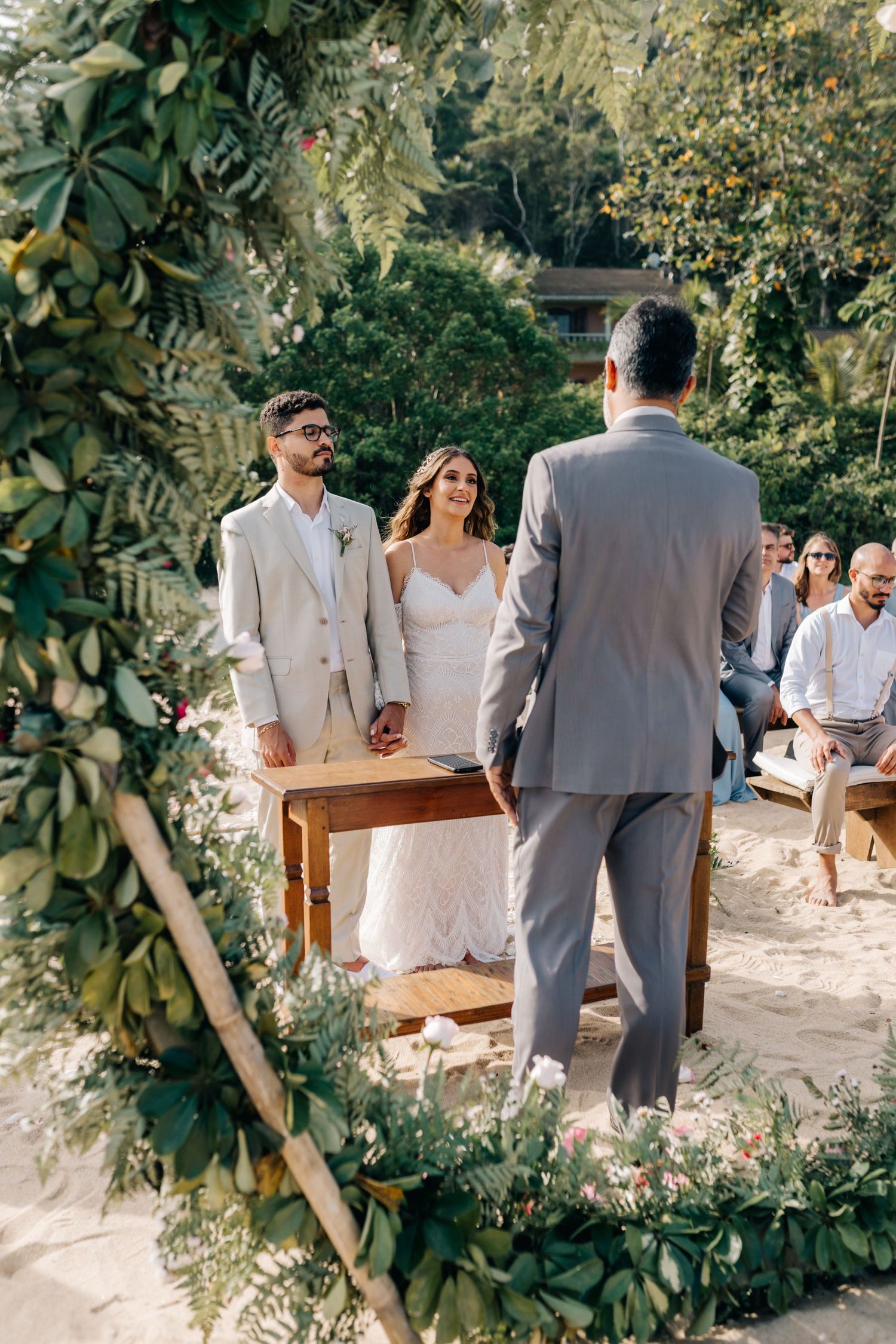 Outdoor wedding ceremony scene with wooden bench and lush green foliage arch.